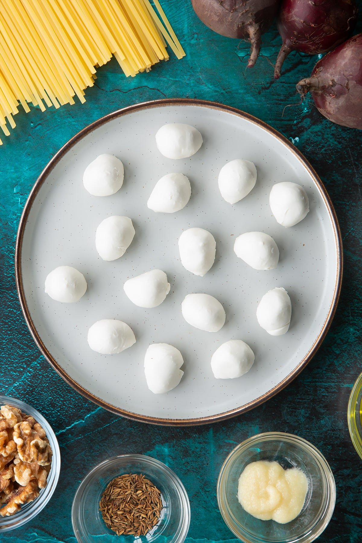 Mozzarella pearls on a plate. Ingredients to make a Halloween pasta recipe surround the plate.