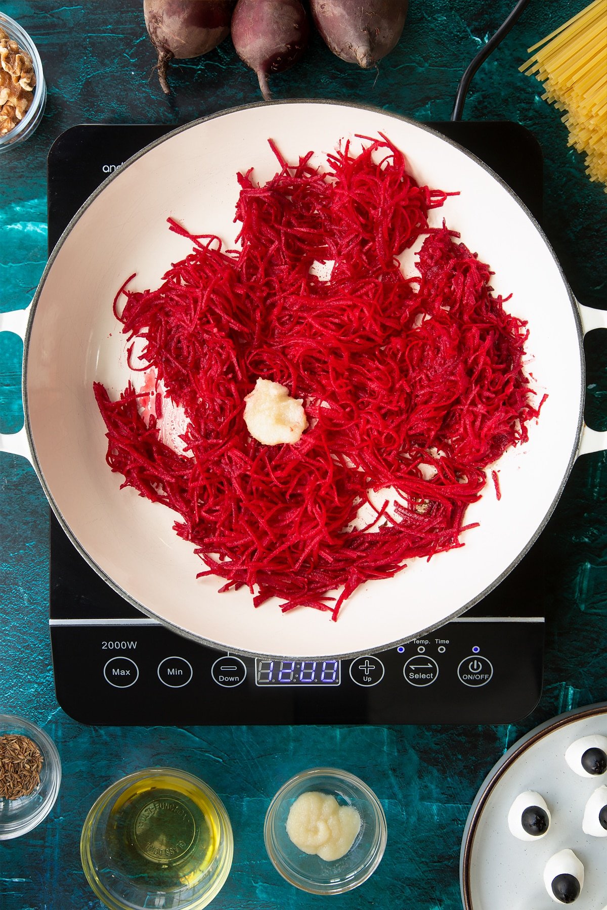 Grated beetroot and garlic in a pan. Ingredients to make a Halloween pasta recipe surround the pan.