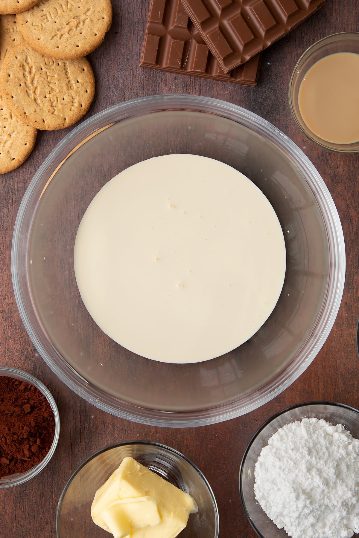 Double cream in a glass bowl. Ingredients to make Baileys cheesecake surround the bowl.