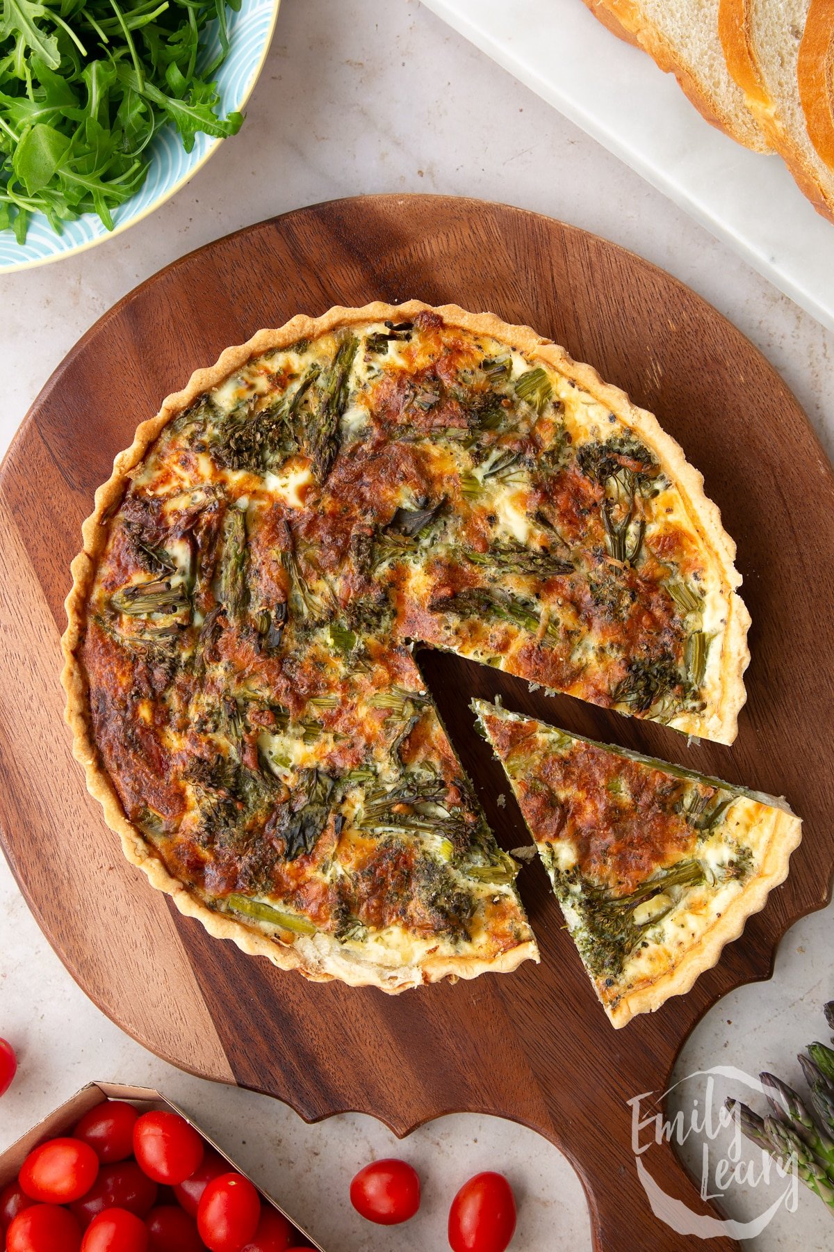 Overhead shot of the finished broccoli and asparagus quiche served on a wooden chopping board.