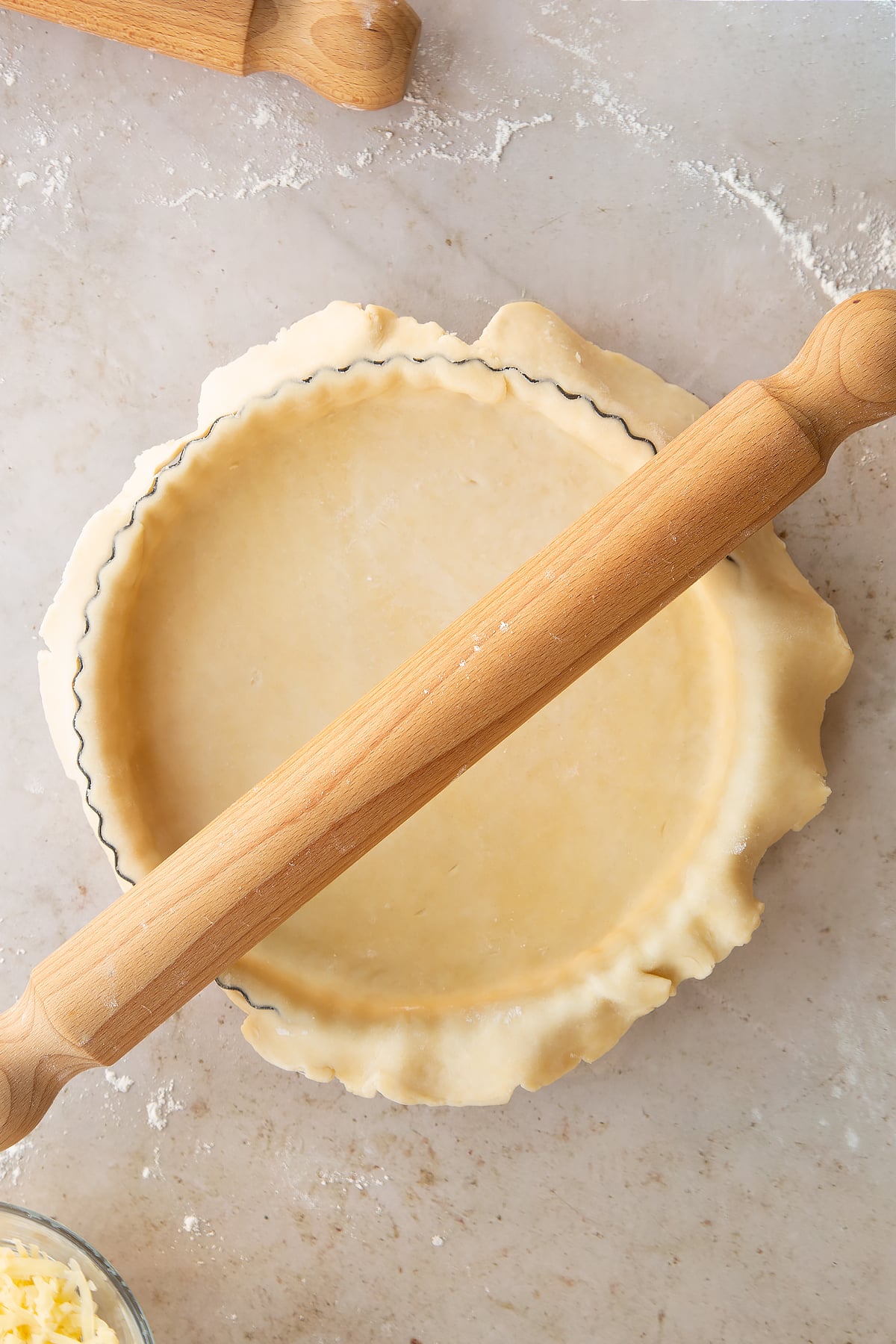 Overhead shot of a rolling pin rolling over the pie tin cutting off the edges for the chestnut quiche pastry casing.