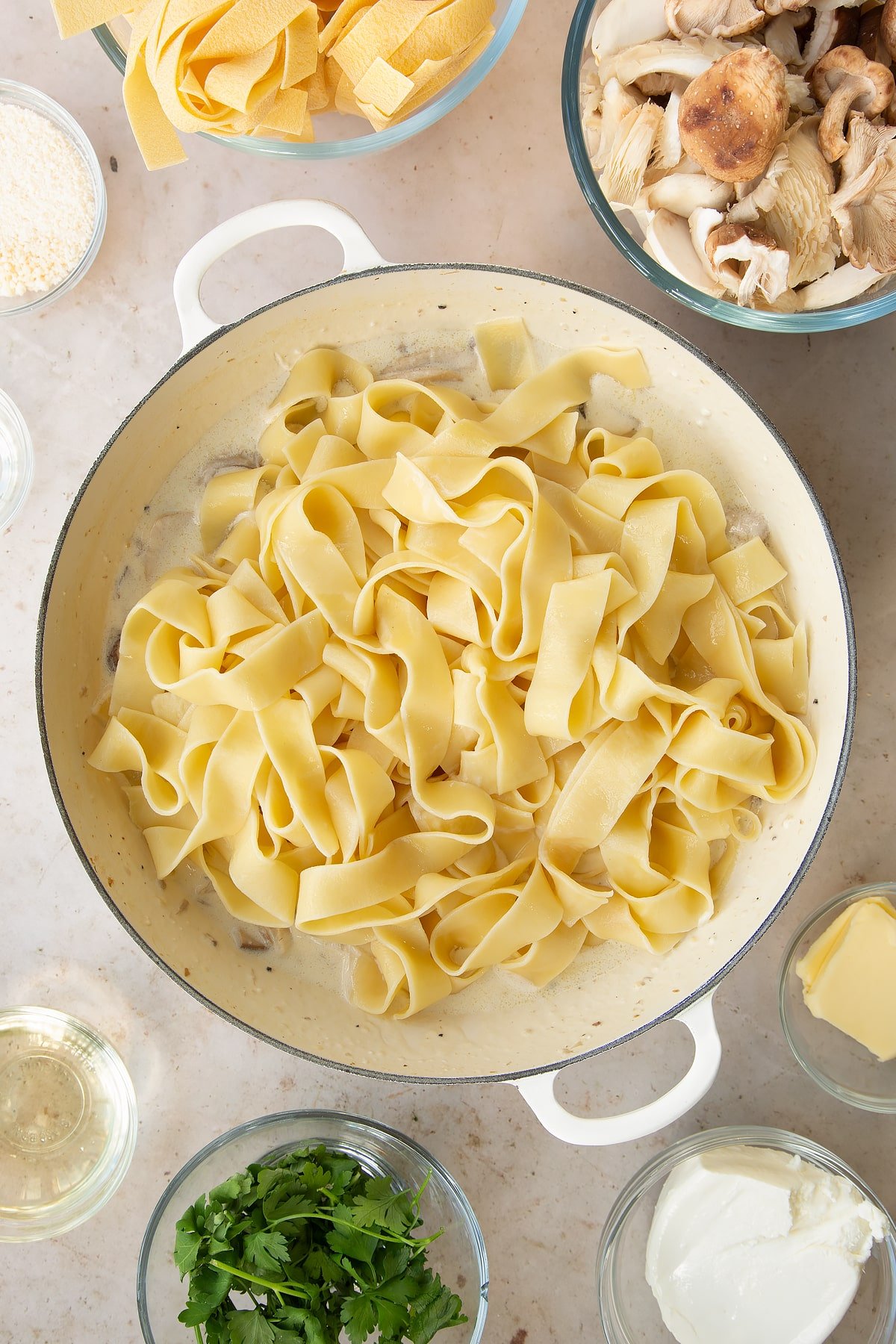 stirred milk and cream cheese sauce with mushrooms topped with cooked fettuccine in a large pan.