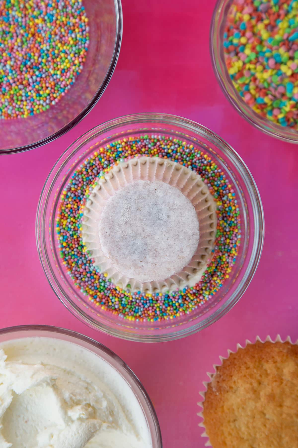 a over head view of a cupcake with frosting, frosting down into a bowl of rainbow sprinkles.