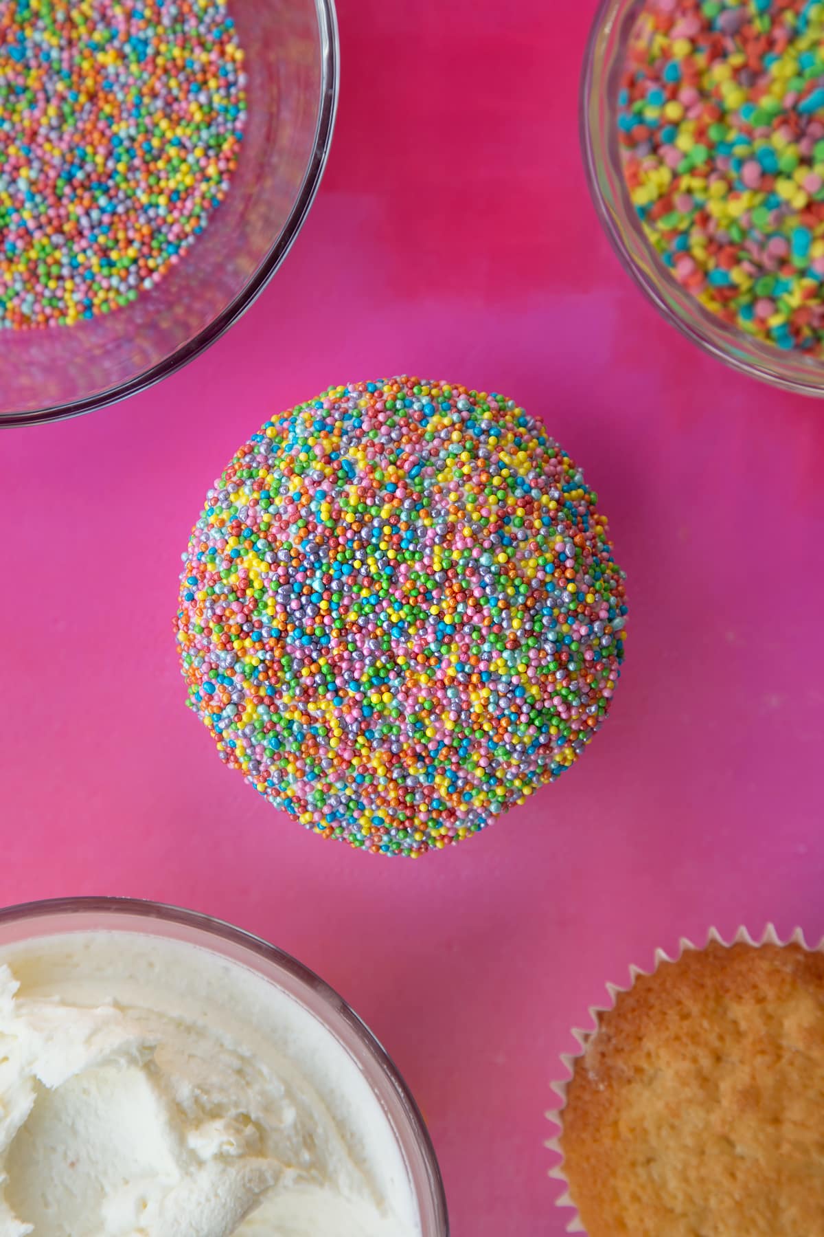 an overhead shot of a cupcake topped with flat frosting covered in rainbow sprinkles.