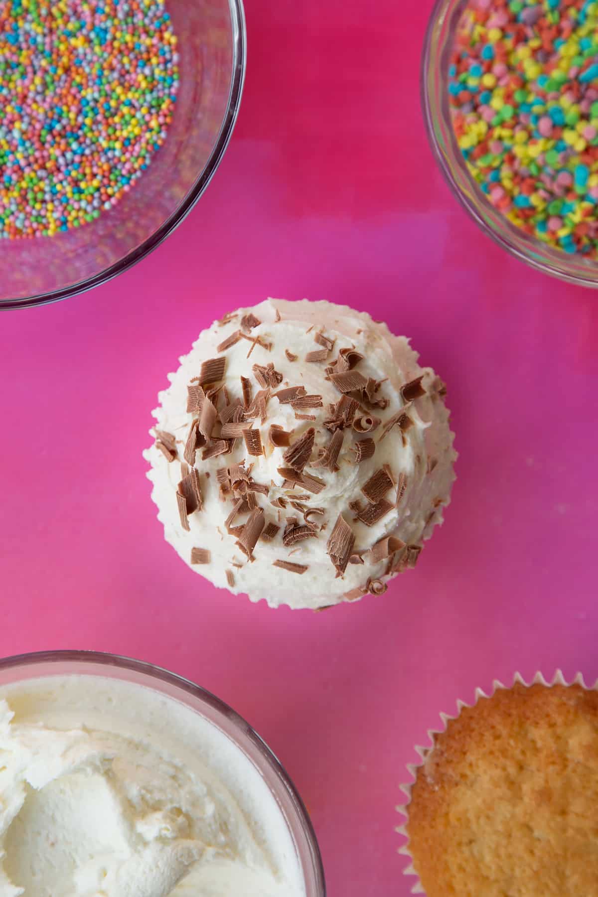 an over head view of a plain sponge cupcake with a swirl of white fosting on topped with chocolate shavings.