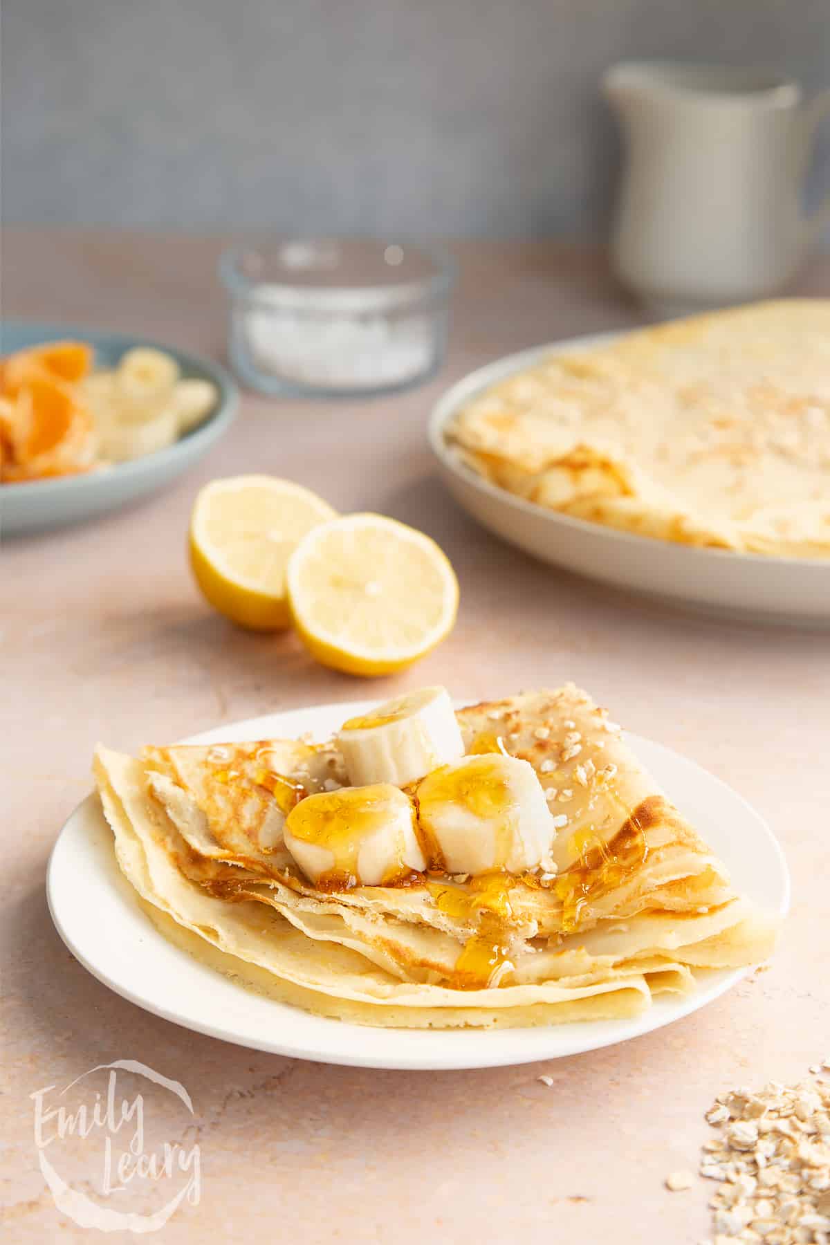 Gluten free crepe on a white plate. It is folded and topped with bananas and golden syrup.