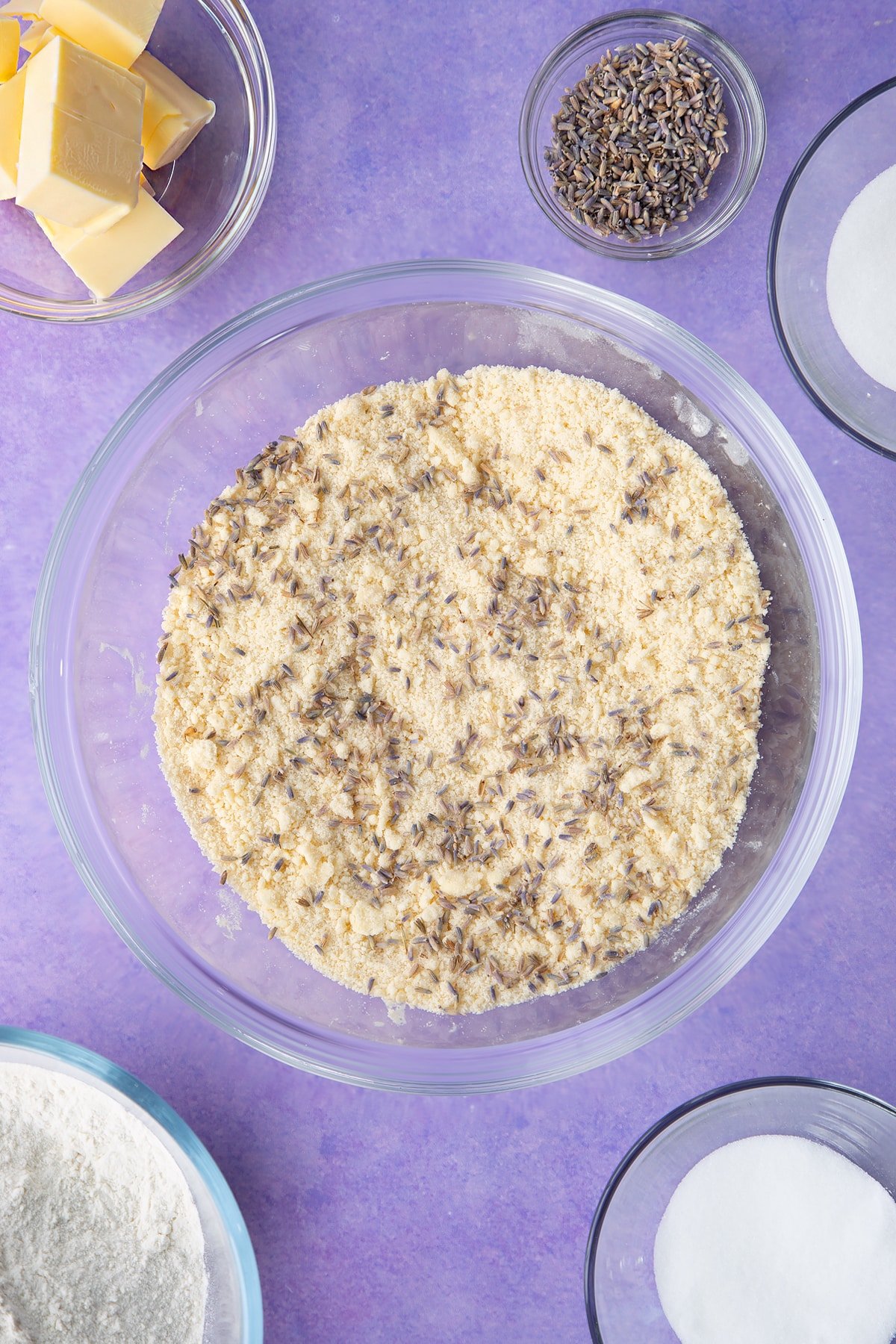 Flour, sugar, butter mixed to a crumb in a bowl with lavender on top. Ingredients to make lavender shortbread cookies.