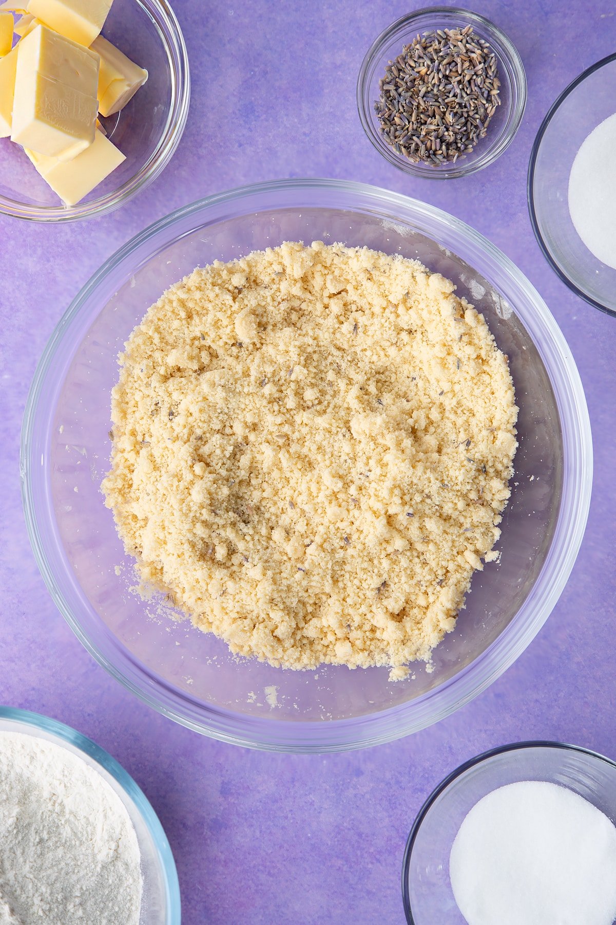 Flour, sugar, butter, lavender and water mixed to a crumb in a bowl. Ingredients to make lavender shortbread cookies.