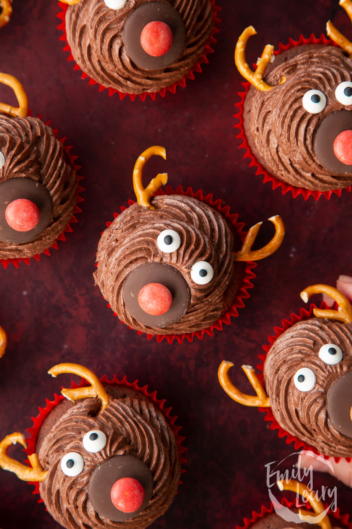 Reindeer cupcakes shown from above on a dark red backdrop.