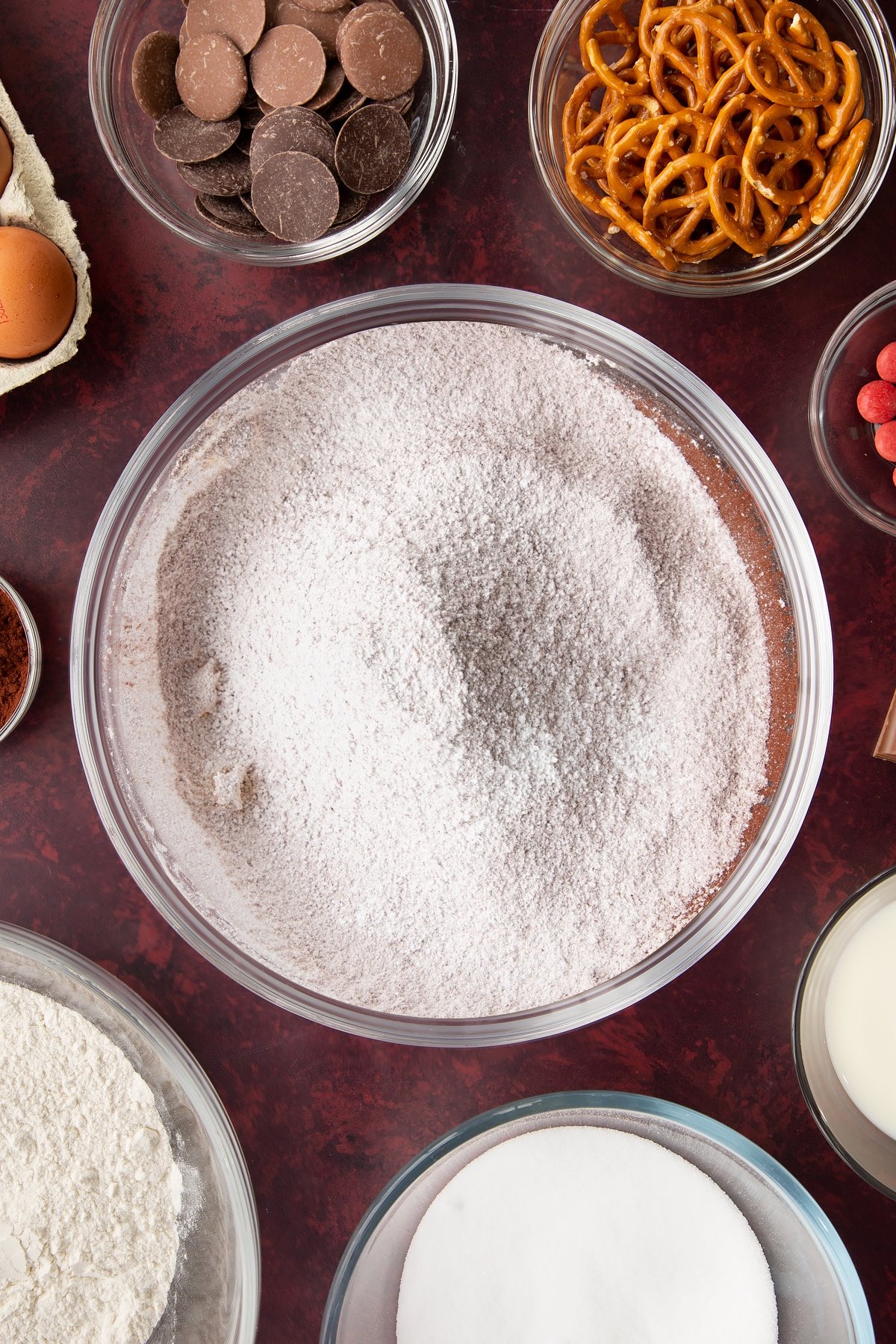 Whipped softened butter, icing sugar, cocoa powder, milk and hot water in a mixing bowl. Ingredients to make reindeer cupcakes surround the bowl.