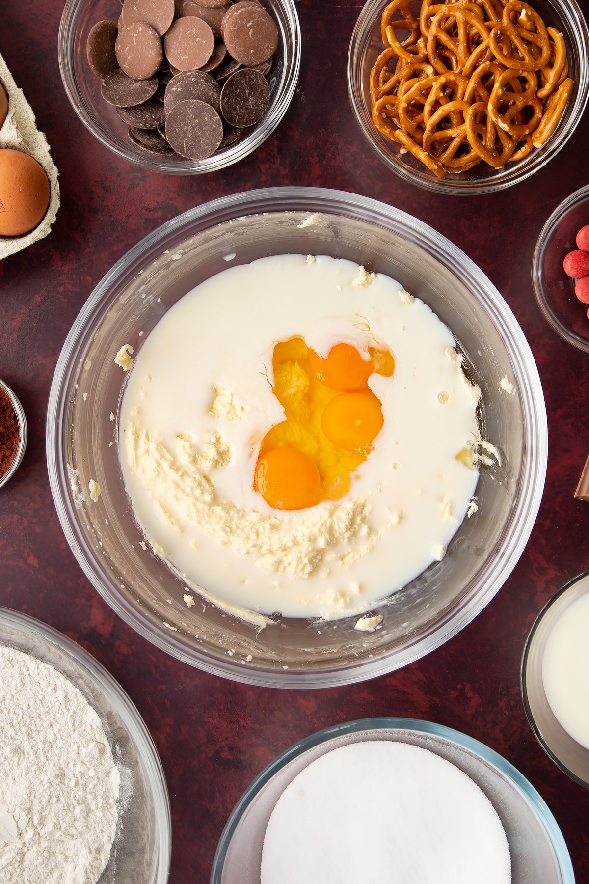 Softened butter and caster sugar beaten together in a mixing bowl with eggs and milk on top. Ingredients to make reindeer cupcakes surround the bowl.