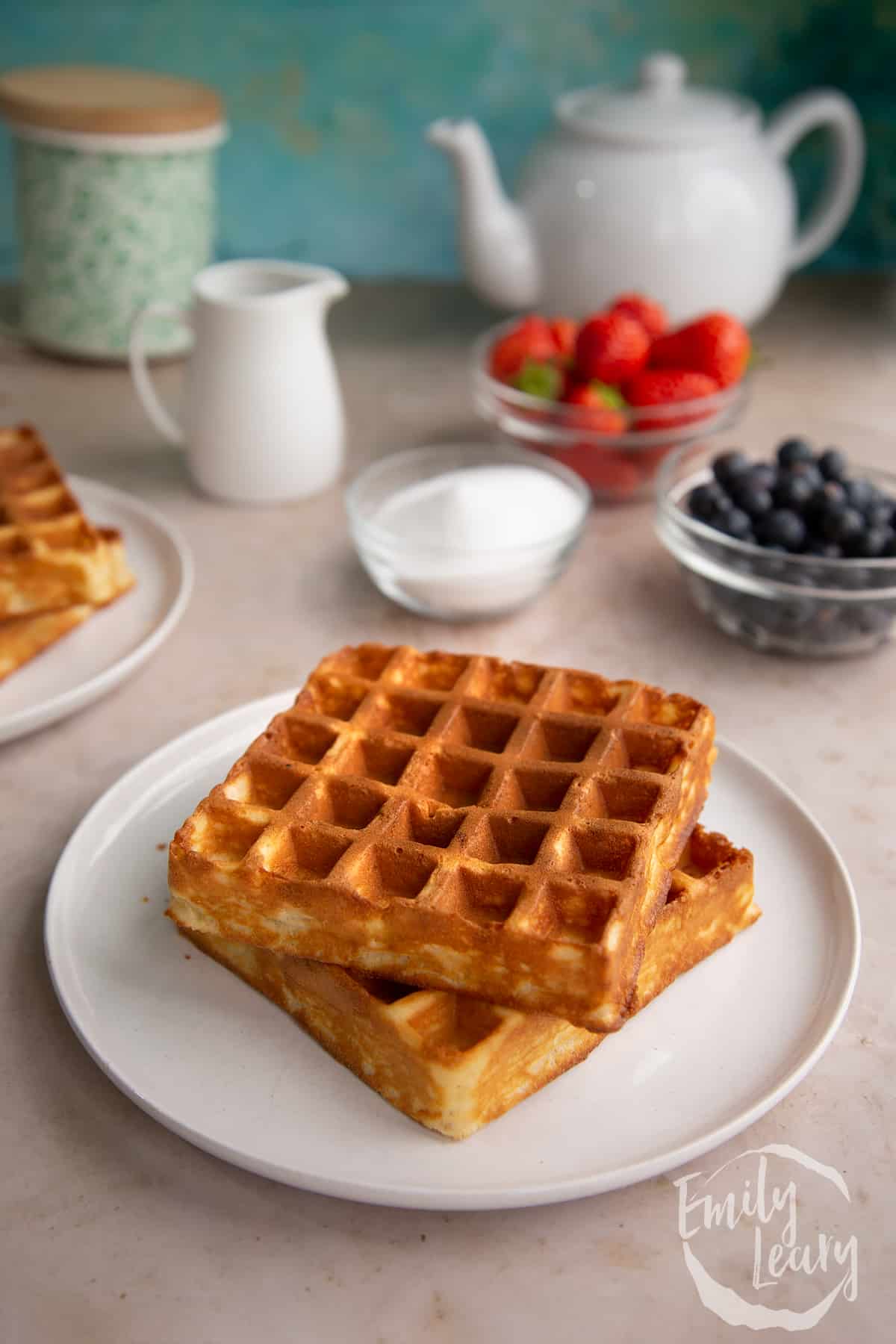 2 cooked waffles stacked on top of each other on a white plate with berries in the background.