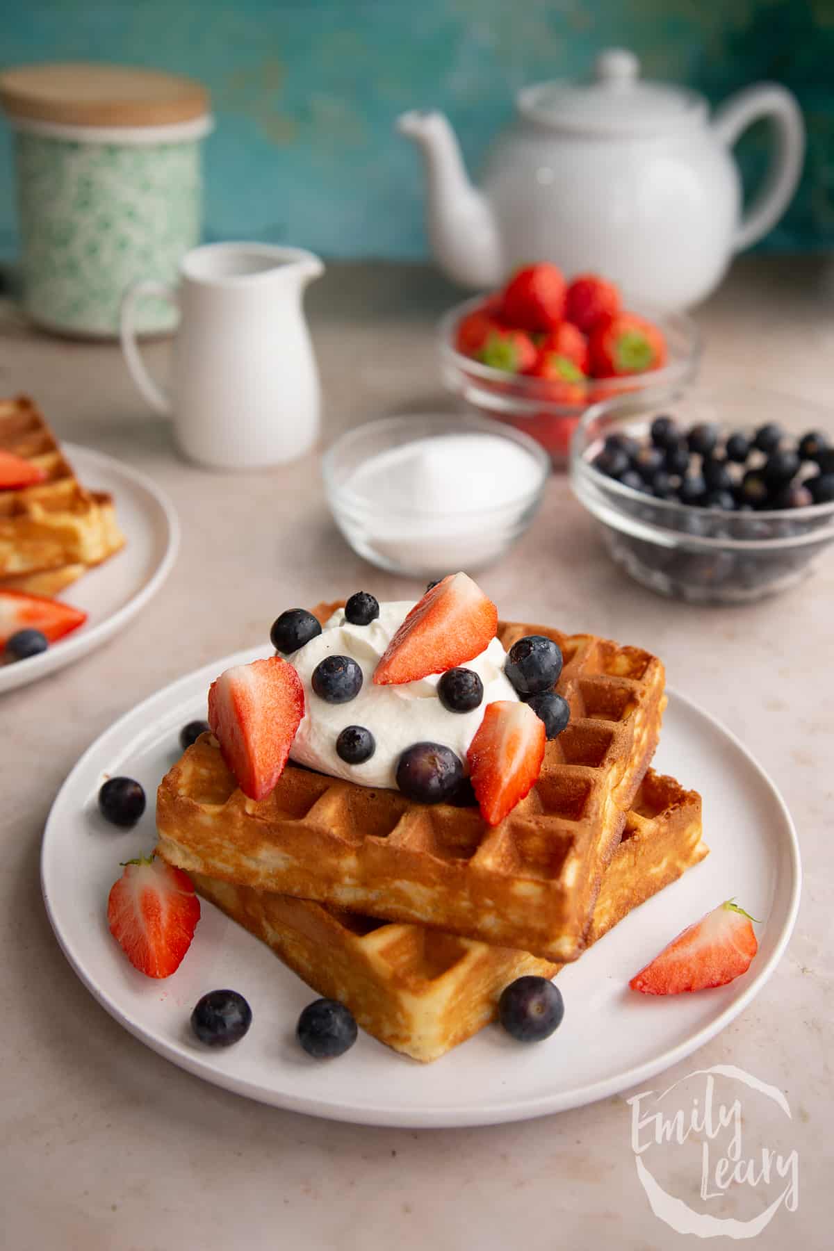 2 cooked waffles stacked on a white plate topped with yogurt, honey and berries.