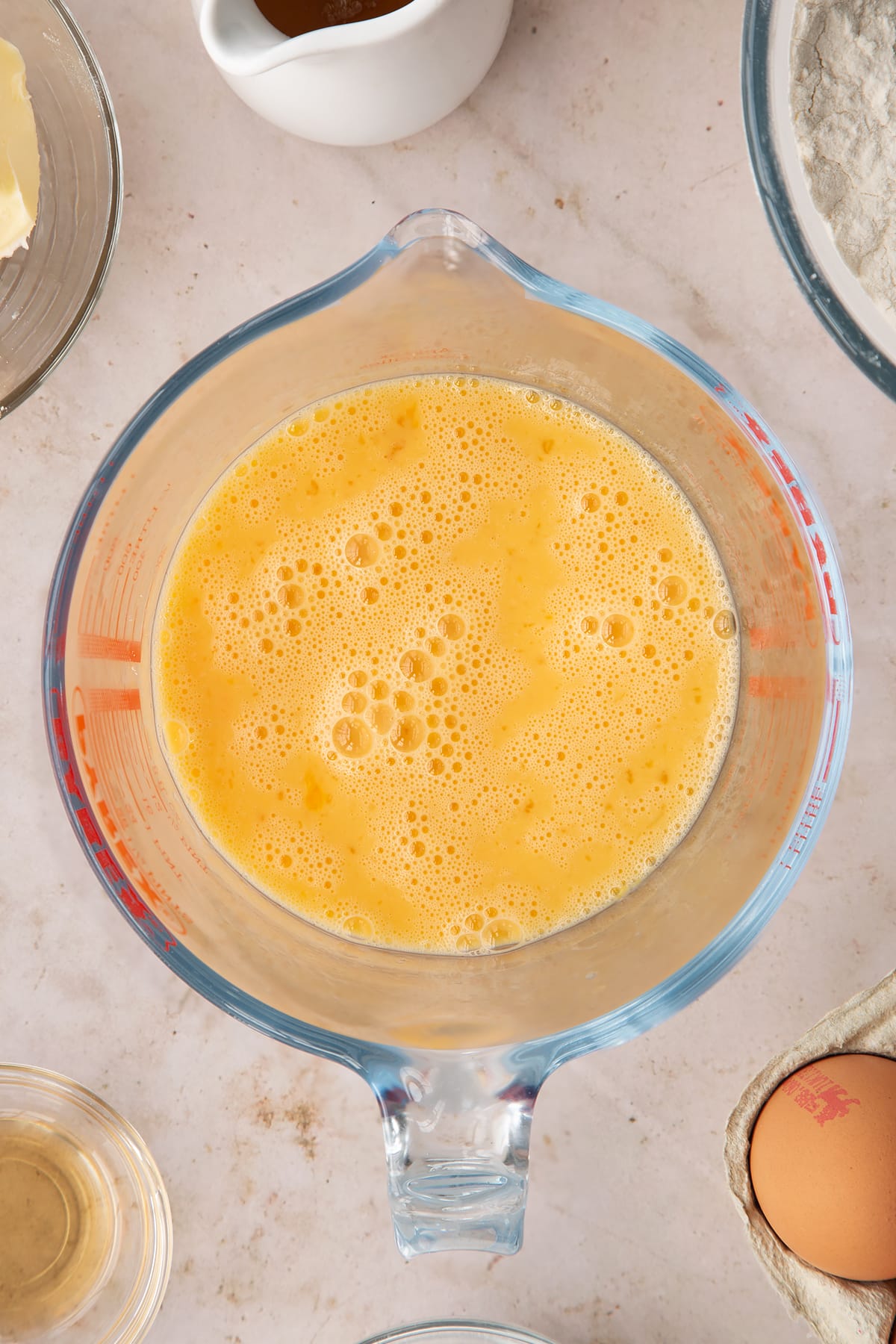 whisked eggs, milk and vanilla in a glass jug on a beige background.