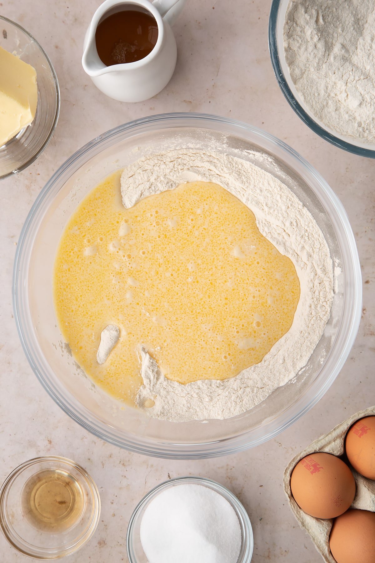 whisked butter, egg and milk mixture poured on top of the flour and sugar mix in a large clear bowl.