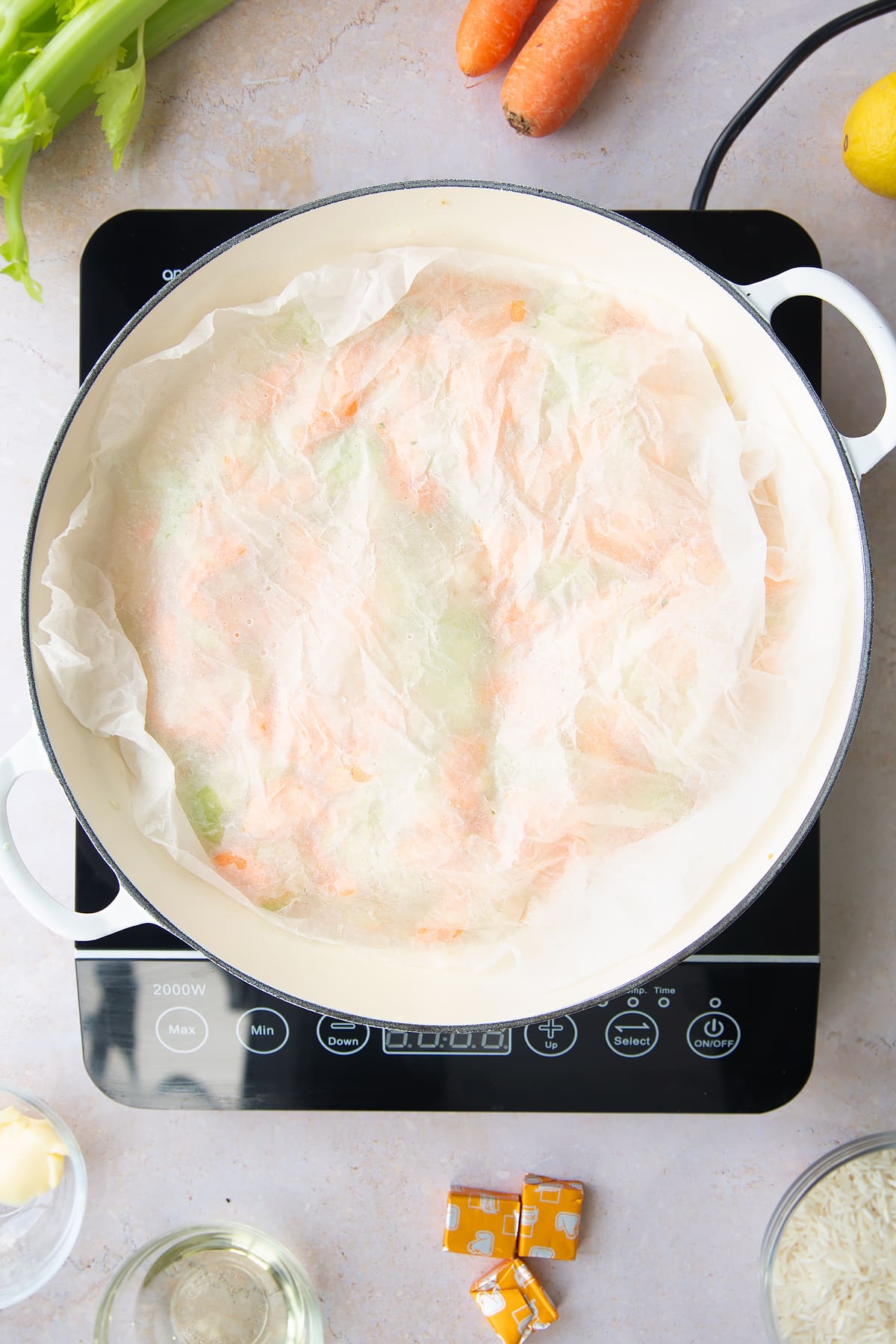 Overhead shot of the baking paper being layered ontop of the diced vegetables for the turkey rice soup inside a pan.