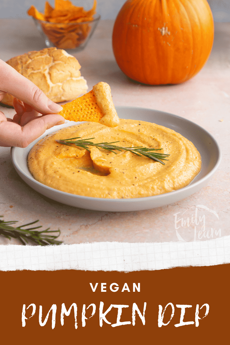 Vegan pumpkin dip in a shallow grey bowl with a sprig of rosemary. A hand dips a tortilla chip into it. Caption reads: Vegan pumpkin dip.