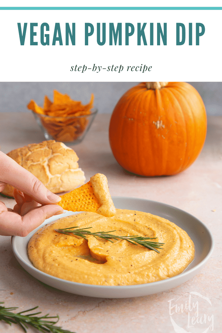 Vegan pumpkin dip in a shallow grey bowl with a sprig of rosemary. A hand dips a tortilla chip into it. Caption reads: Vegan pumpkin dip. Step-by-step recipe.