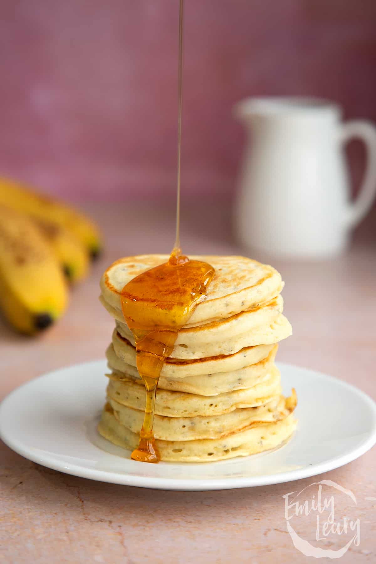 A stack of vegan chia pancakes on a small white plate. They are being drizzled with golden syrup. 