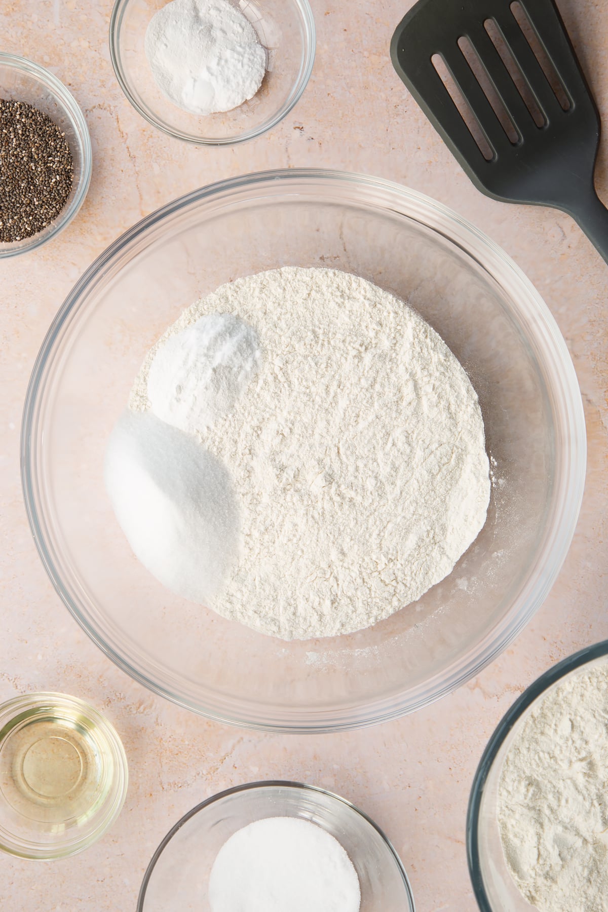 Self-raising flour, sugar, baking powder and bicarbonate of soda in a bowl. Ingredients to make vegan chia pancakes surround the bowl.