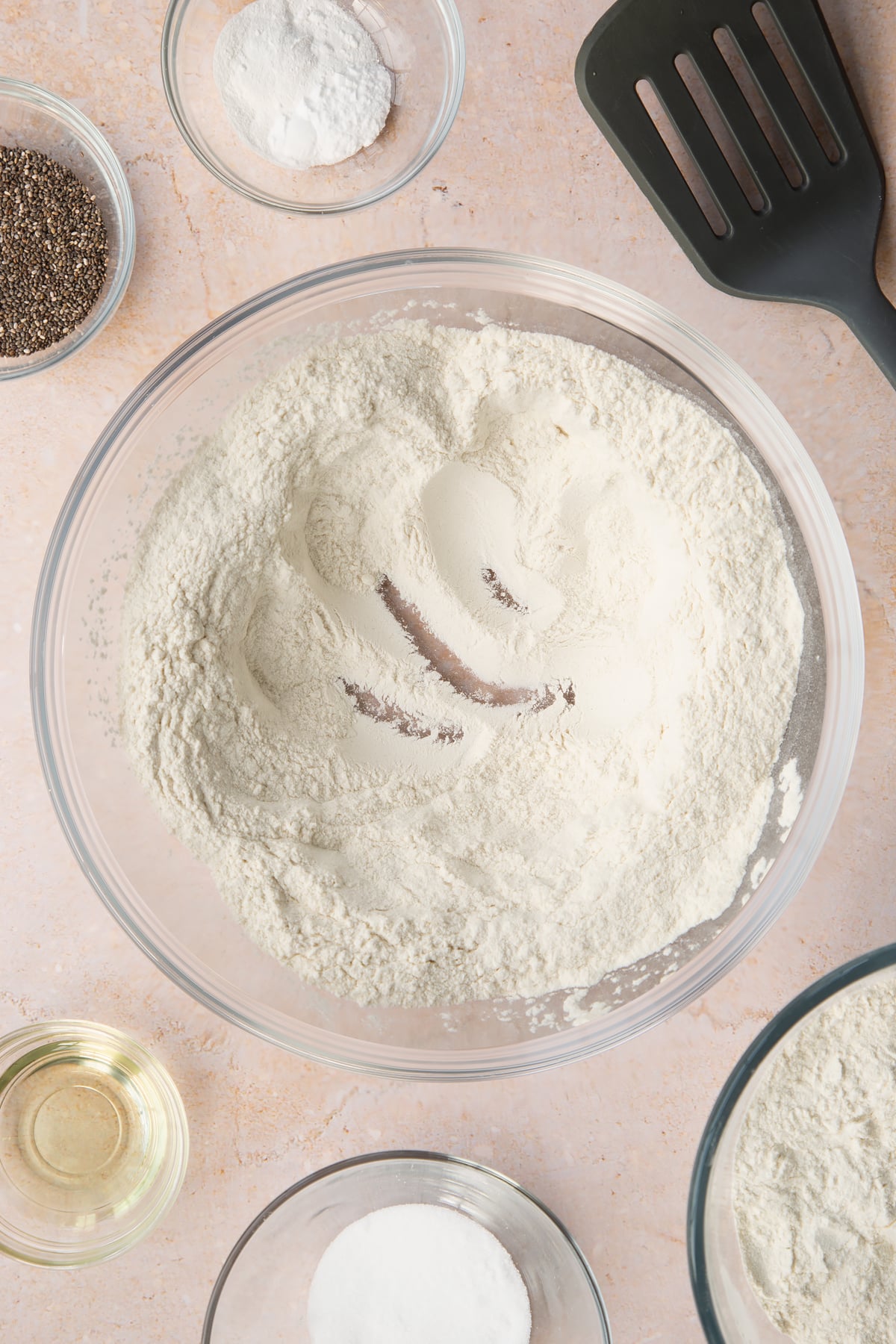 Self-raising flour, sugar, baking powder and bicarbonate of soda in a bowl with a well in the centre. Ingredients to make vegan chia pancakes surround the bowl.