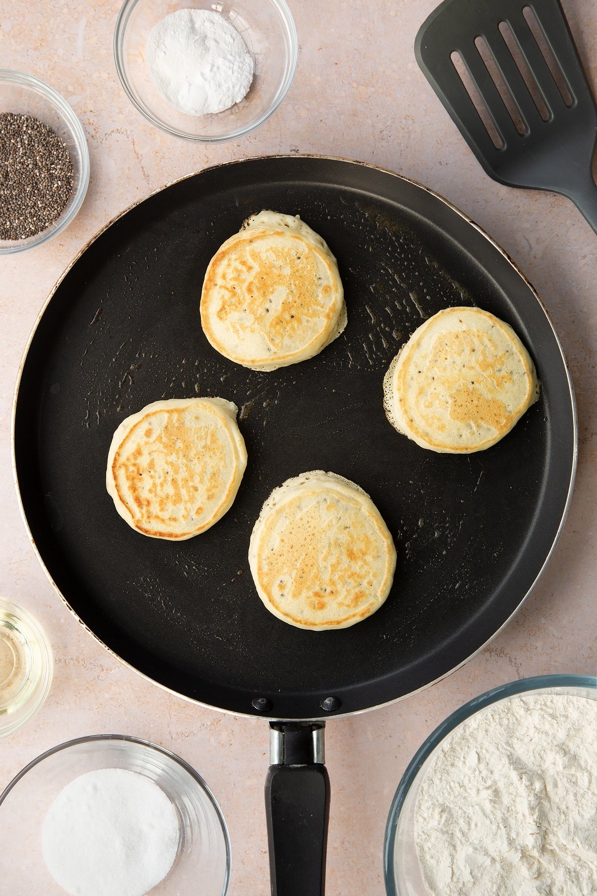 A pancake pan with four vegan chia pancakes, half cooked and flipped.