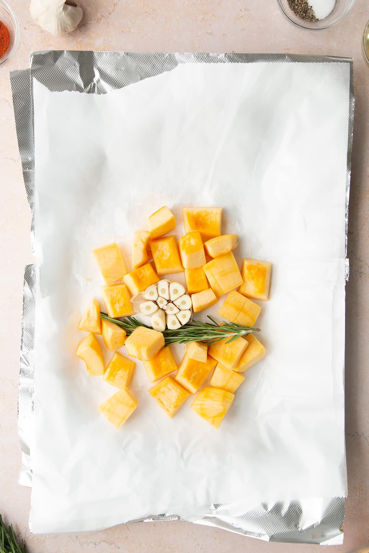 Chopped pumpkin, garlic and rosemary on layers of paper and foil packet on a baking tray. 