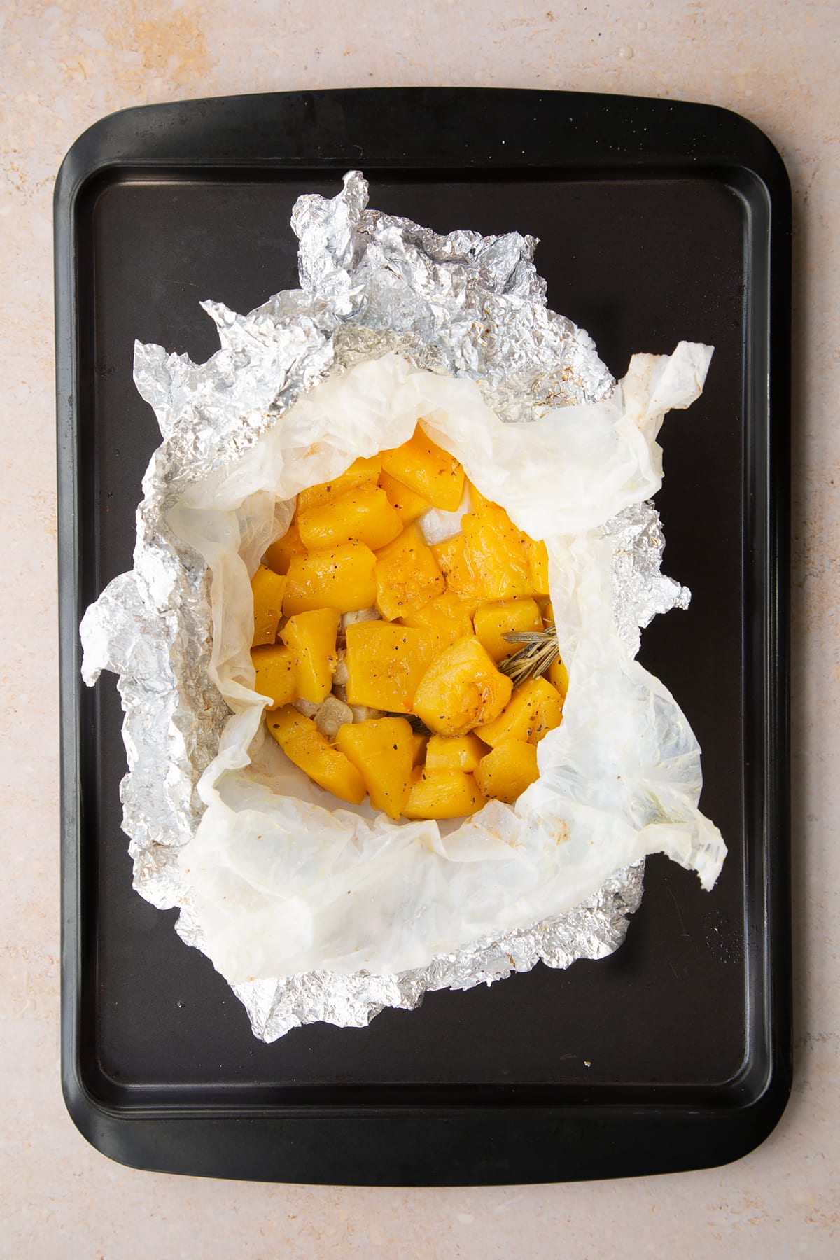 Roasted pumpkin and garlic in a half open paper and foil packet on a baking tray.