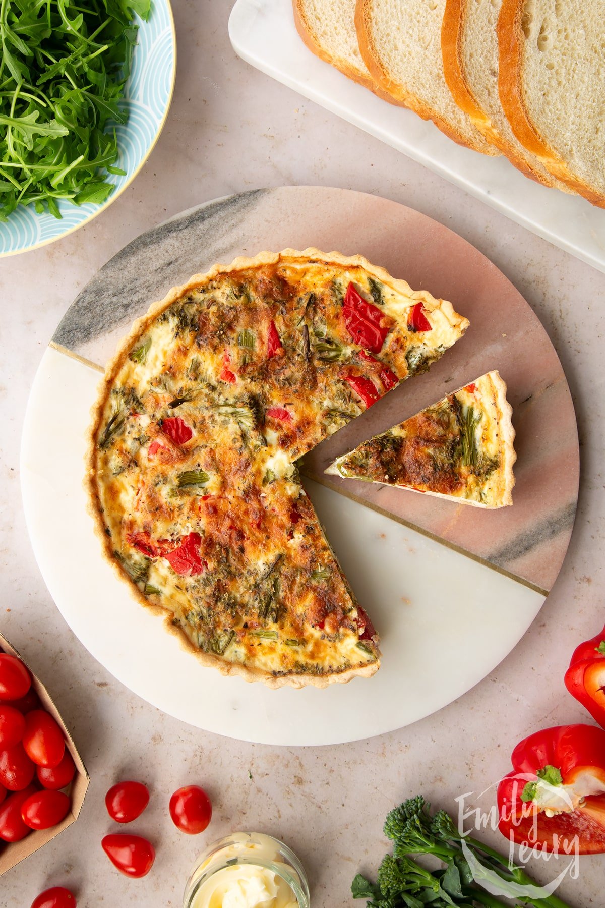 Overhead shot of broccoli and pepper quiche on a circluar serving plate with slices cut out.