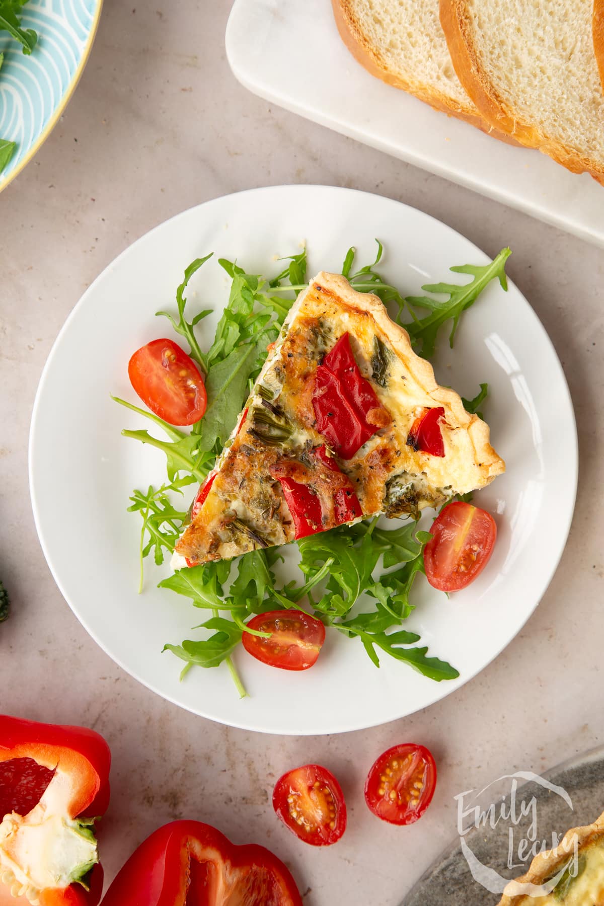 A slice of broccoli and pepper quiche on a bed of salad ontop of a white plate.