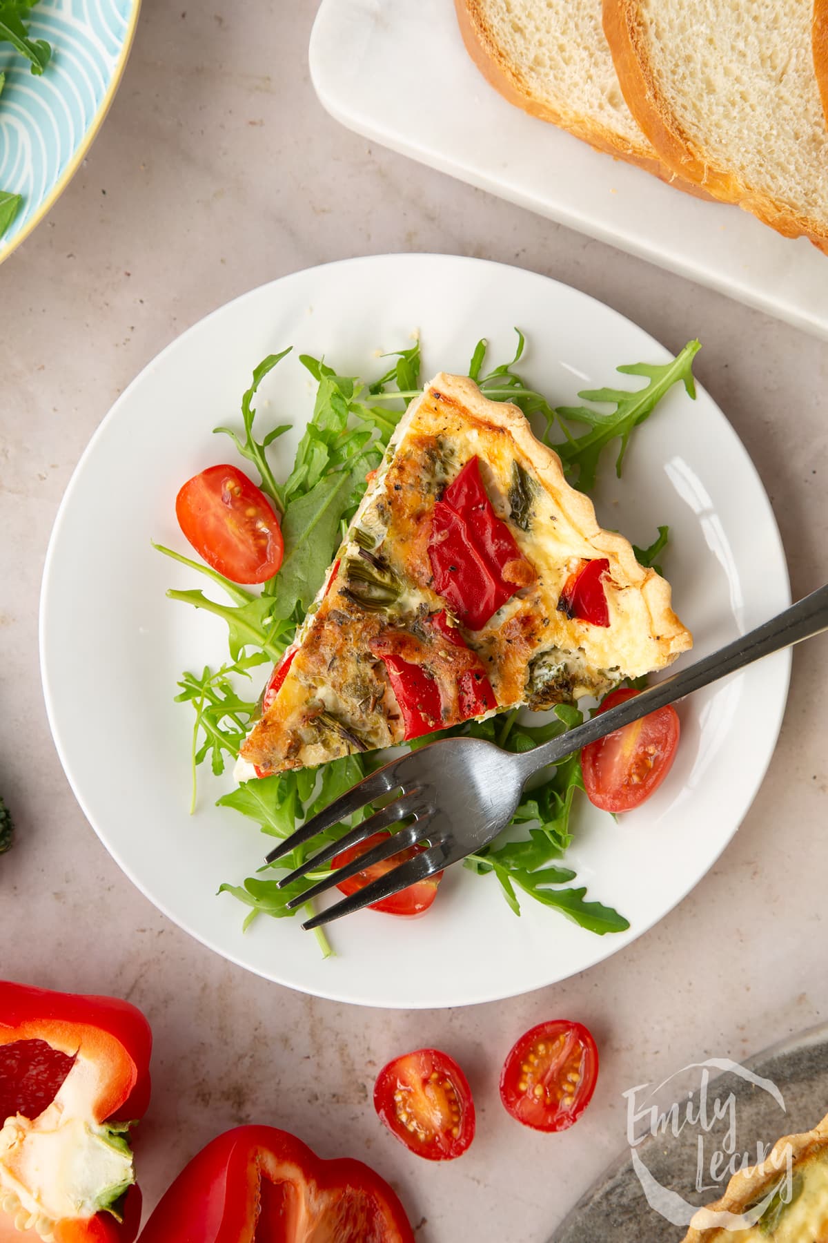 A slice of broccoli and pepper quiche served on a bed of salad with a fork on the side.
