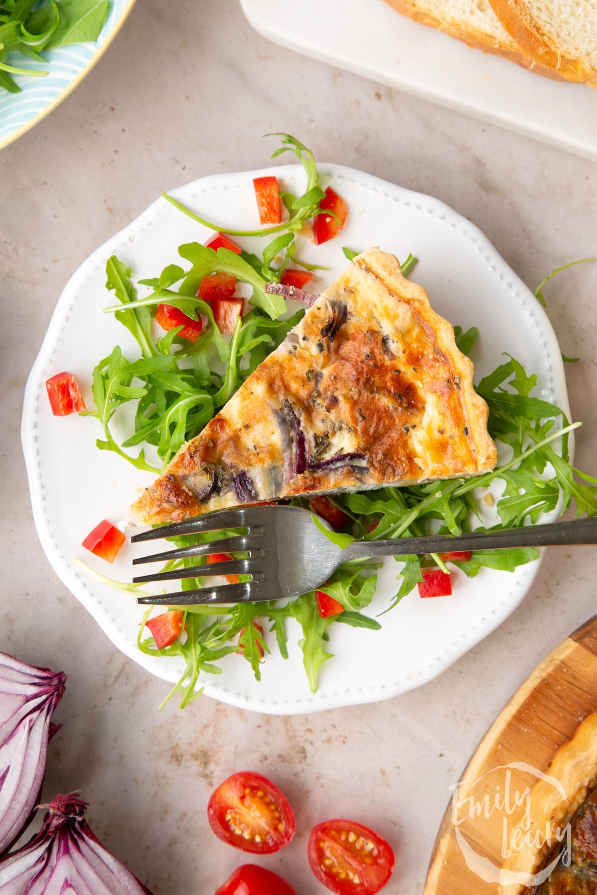 Overhead shot of a slice of chestnut quiche served on a bed of salad on a white decorative plate with a fork at the side.