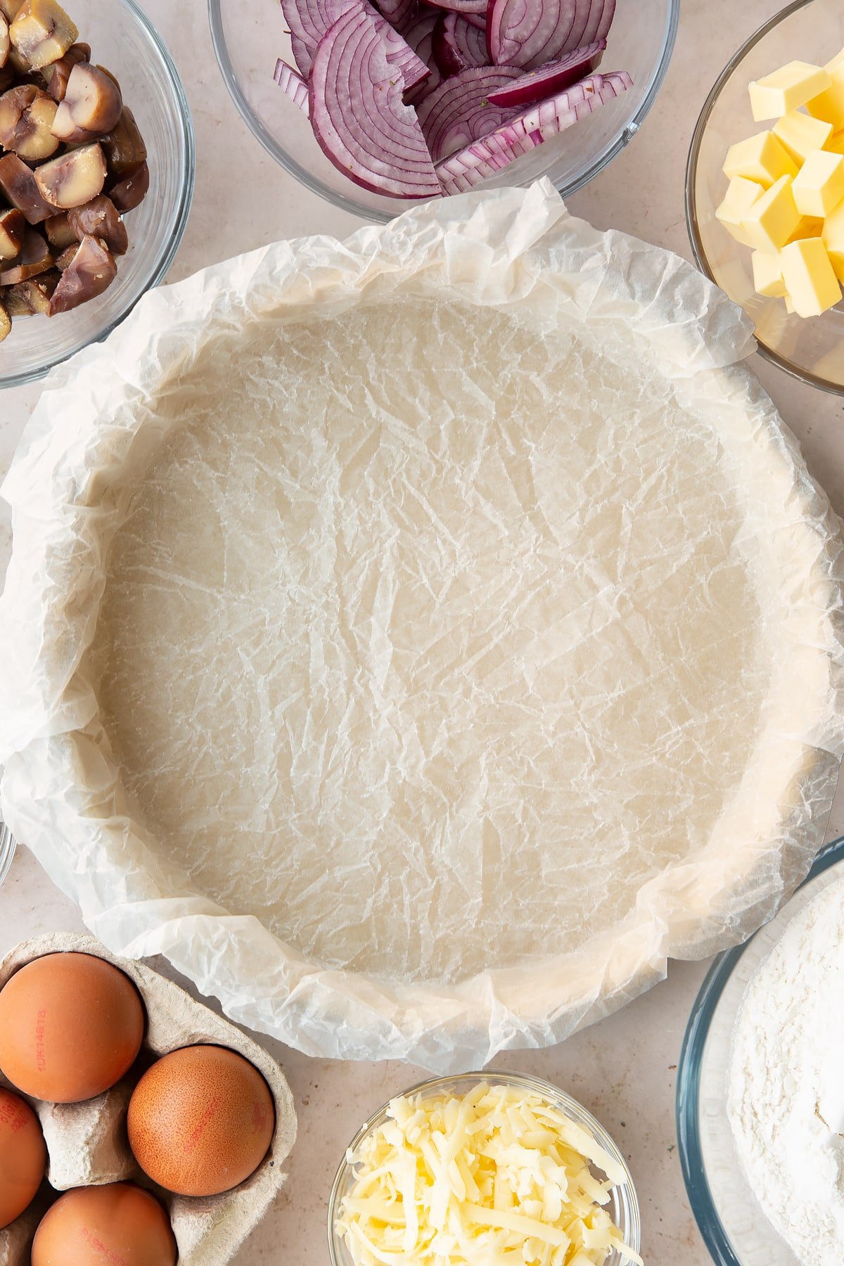 Overhead shot of some baking paper laid over the top of the pastry in a pie tin. 