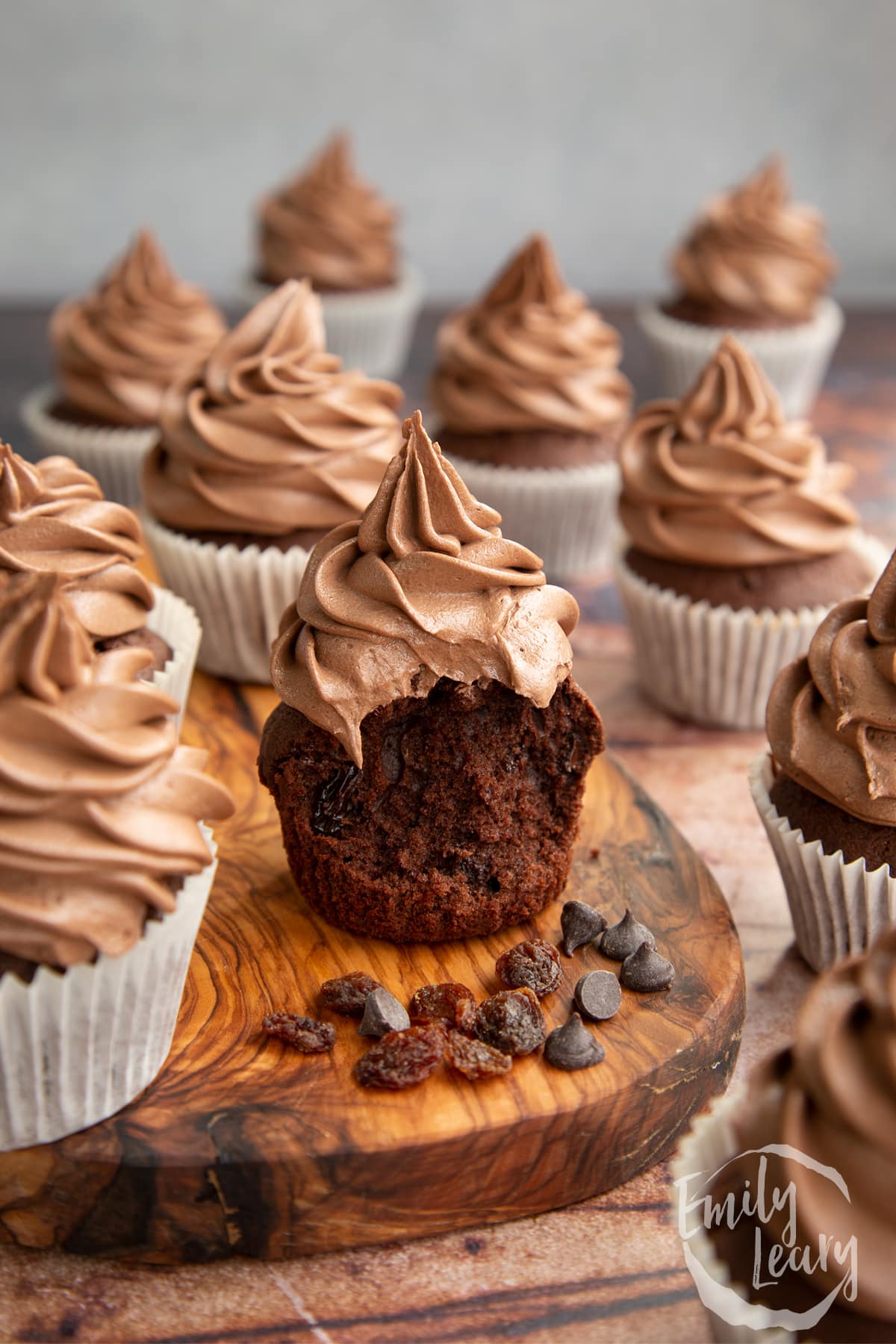 Chocolate raisin muffins with Nutella frosting on a wooden board. The muffin in the fore is unwrapped with a bite out of it. 