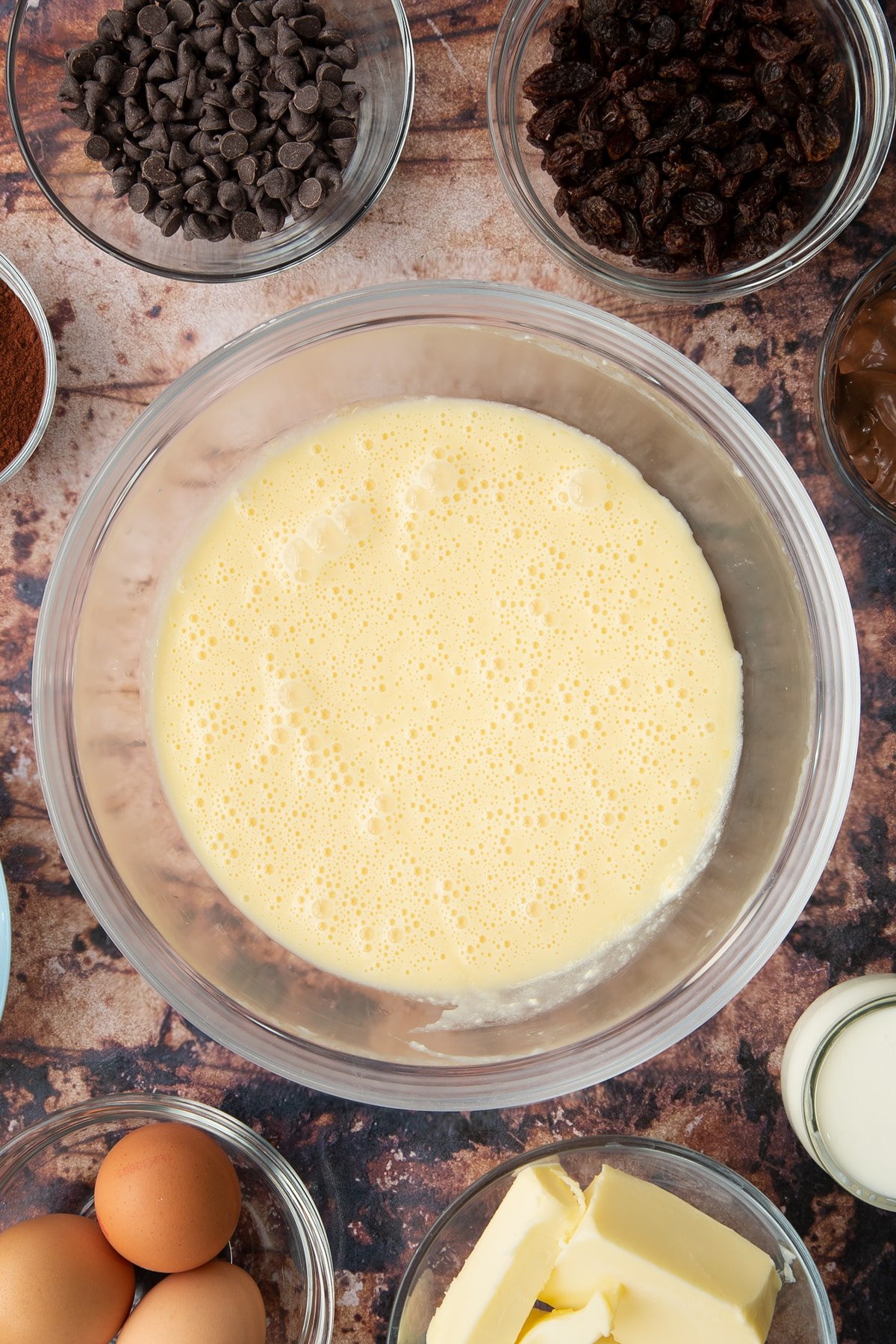 Butter, oil, sugar and eggs in a bowl. Ingredients to make chocolate raisin muffins surround the bowl.