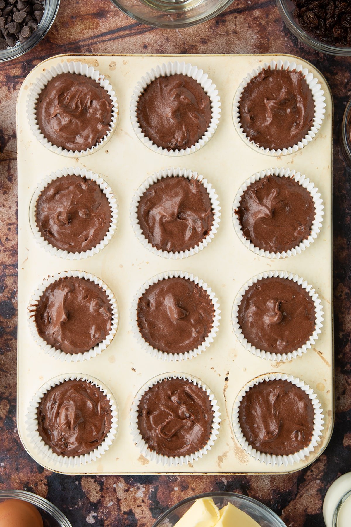 Chocolate raisin muffin batter in cupcake cases in a tray.