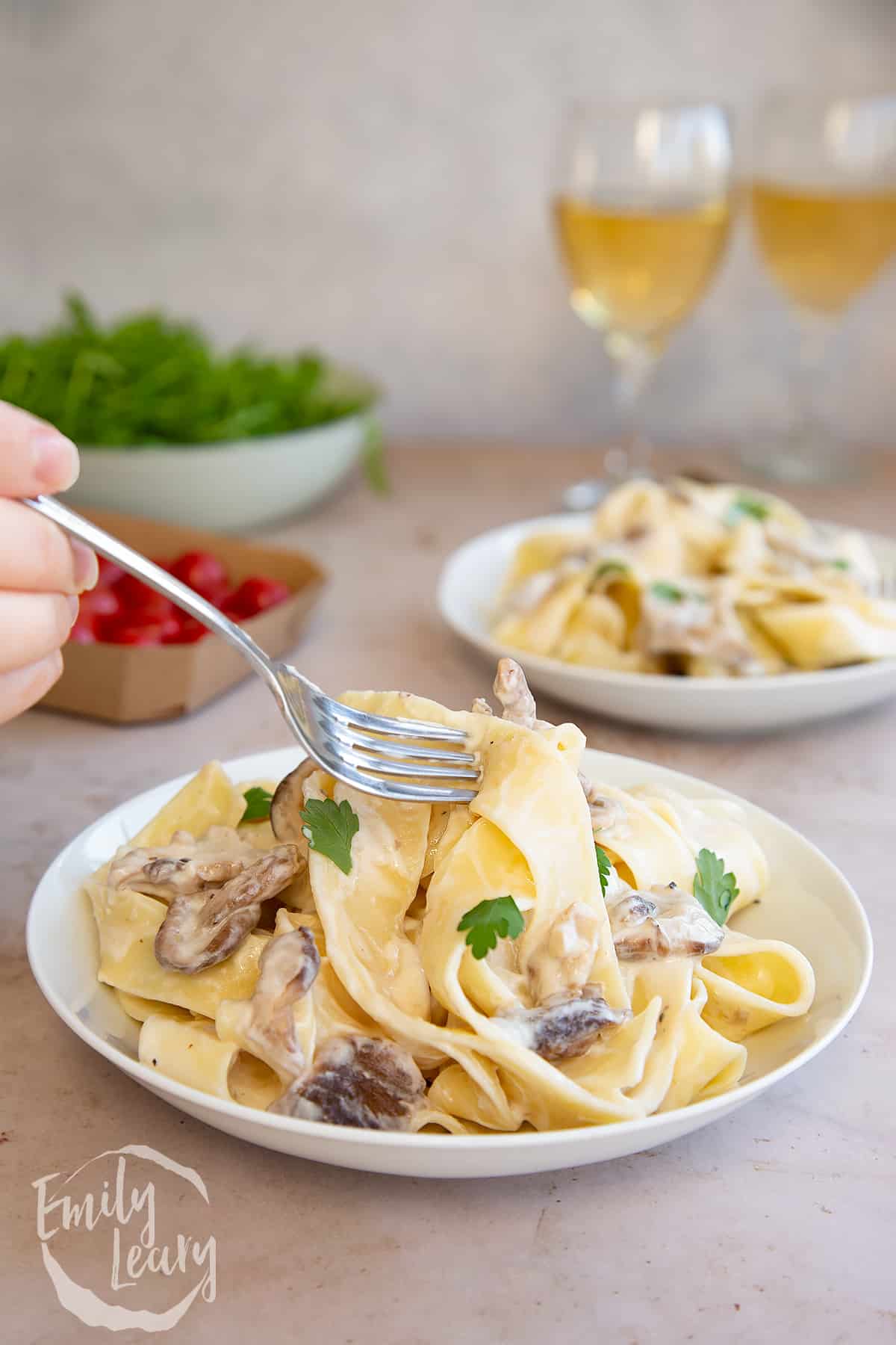 a fork picking up a bite of Creamy mushroom pappardelle from a white bowl on a light surface.