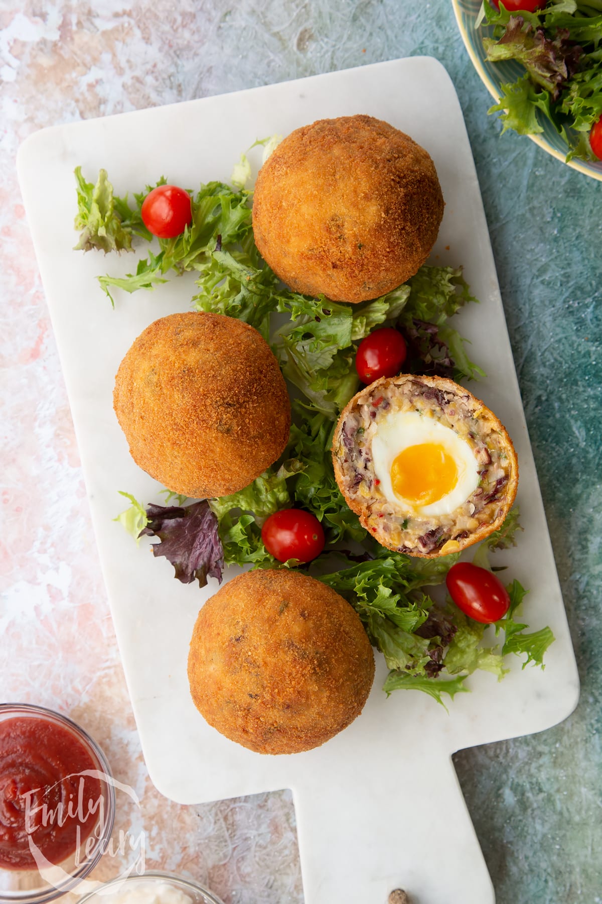 over head shot of a vegetarian scotch egg cut in half on a bed of salad on a white plate with whole scotch eggs.