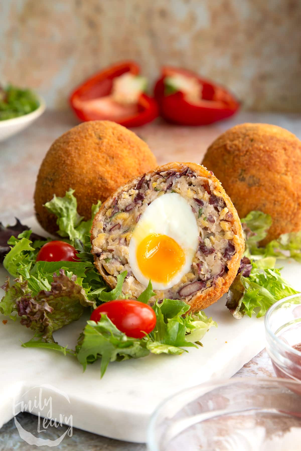 a vegetarian scotch egg cut in half on a bed of salad on a white plate.