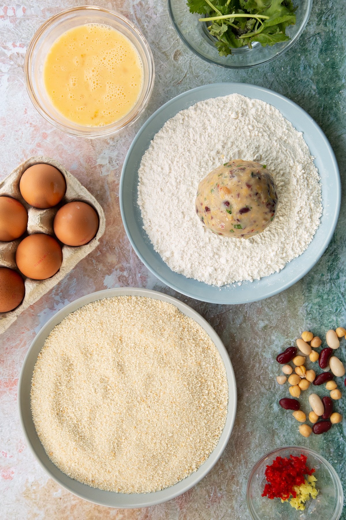 a vegetarian stuffing ball sat in a bowl of flour along teh side of flour and breadcrumbs.