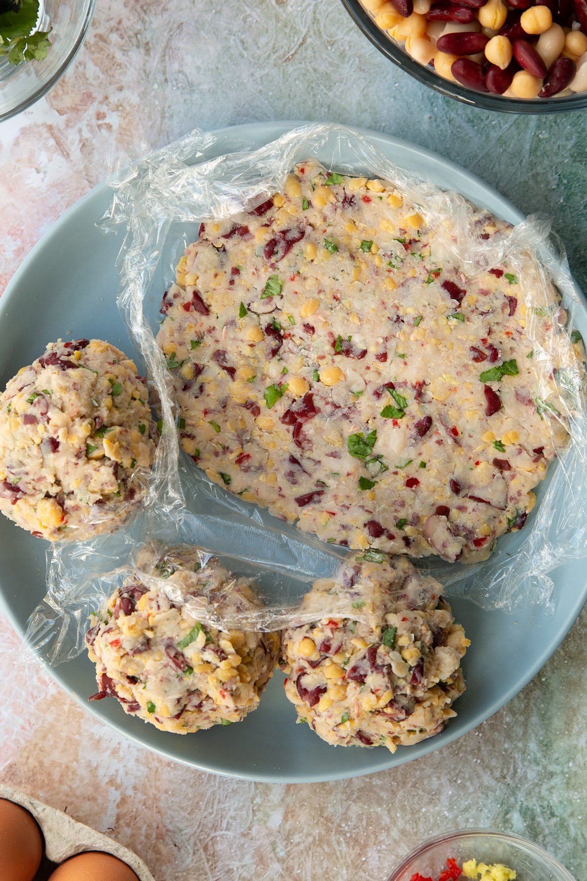 a piece of cling film with a flattened vegetarian ball of stuffing rolled out to create a flat circle on a blue plate.