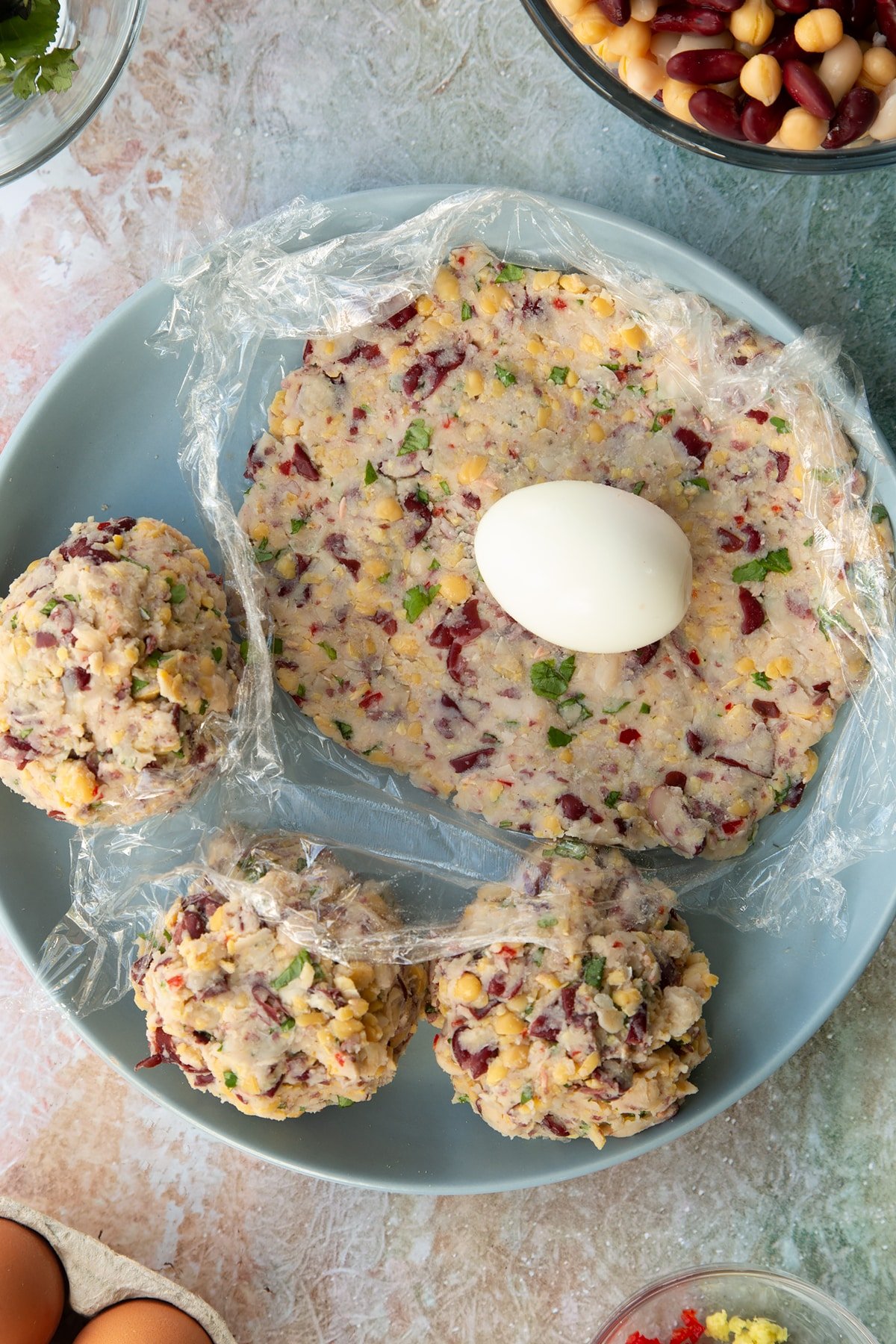 a piece of cling film with a flattened vegetarian ball of stuffing rolled out to create a flat circle on a blue plate topped with a cooked whole egg.