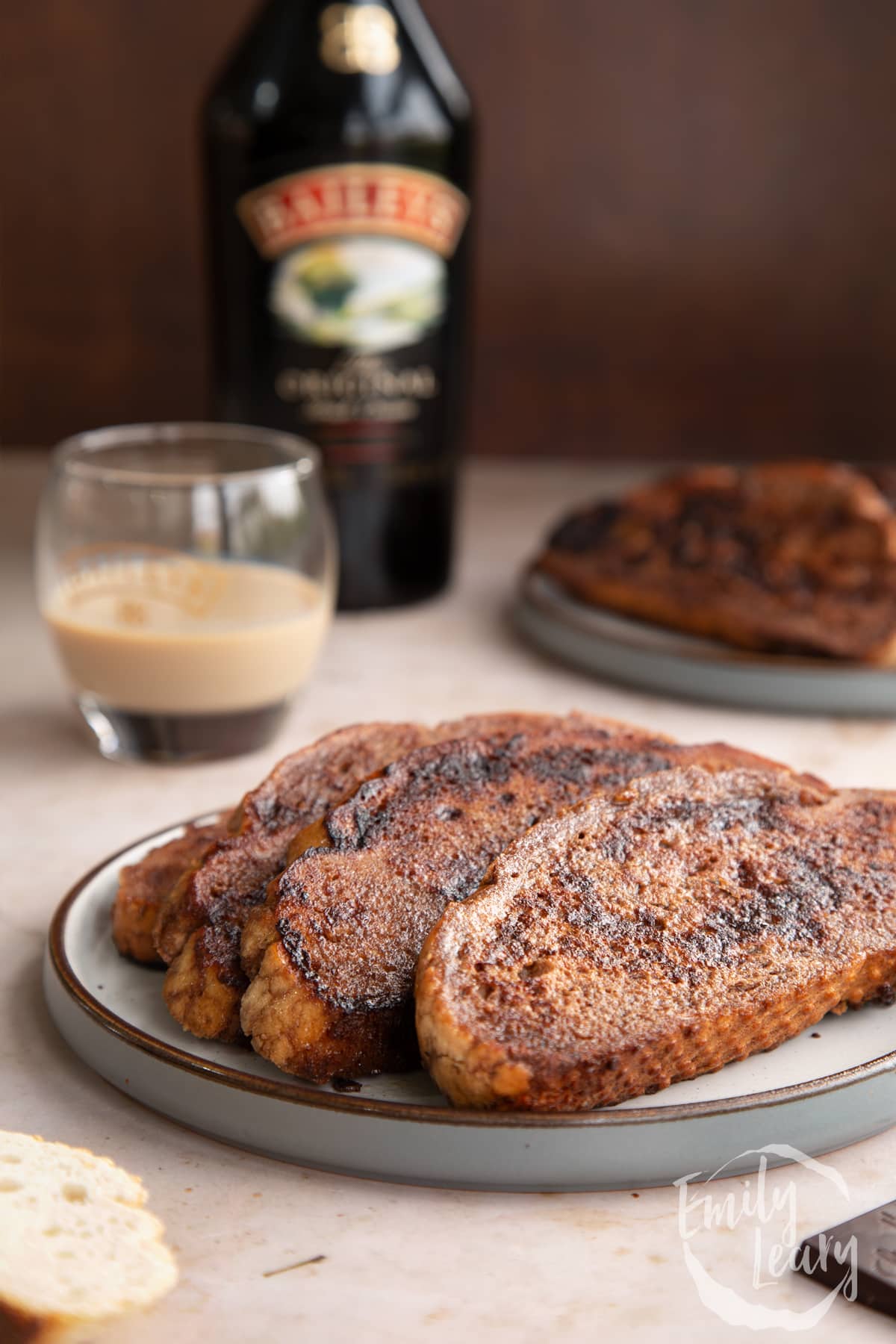 Close up shot of three slices of Baileys French toast on a decoative plate with a glass and bottle of Baileys in the background.