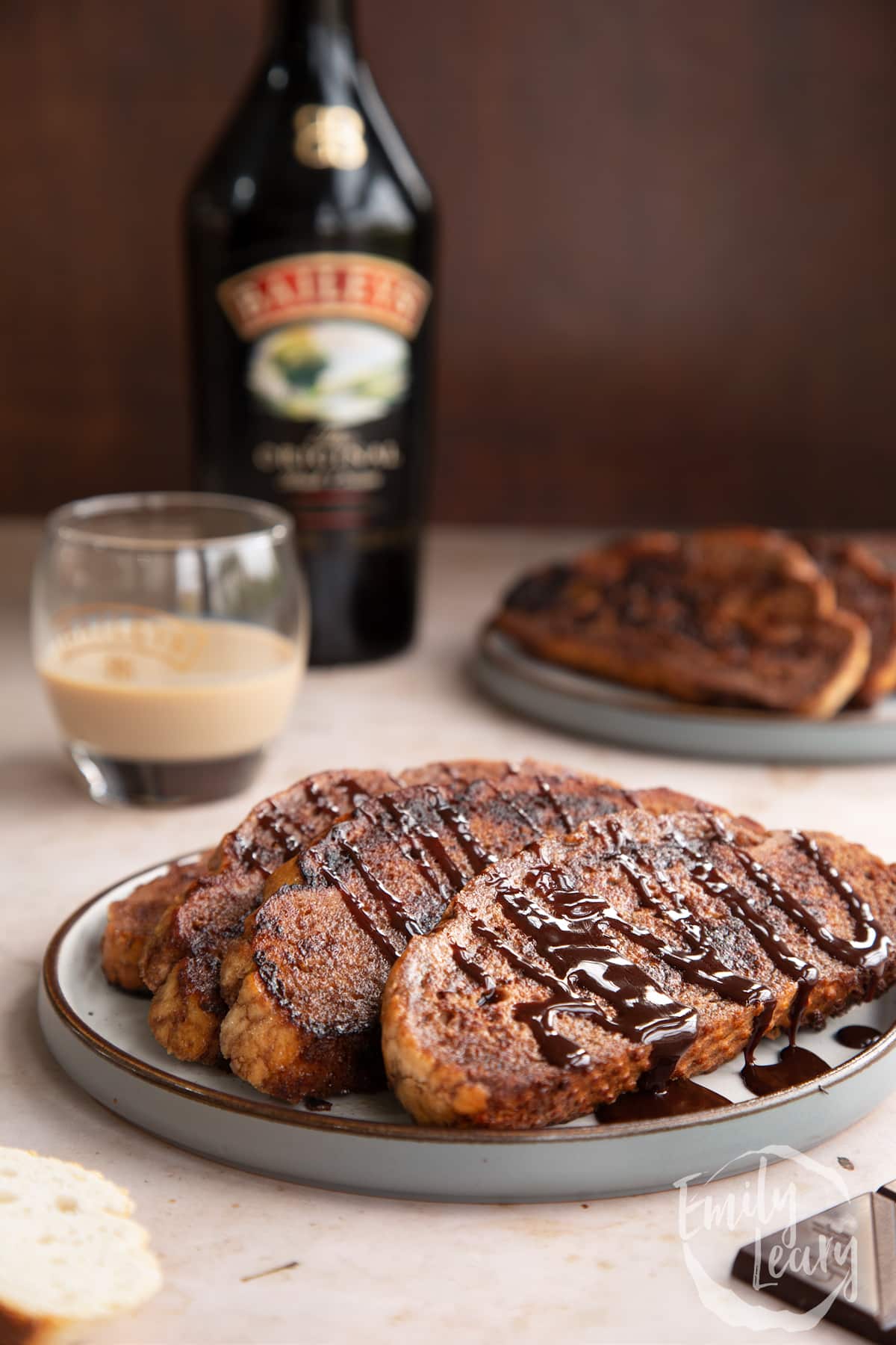Close up shot of three slices of Baileys French toast on a decoative plate with a glass of Baileys in the background.