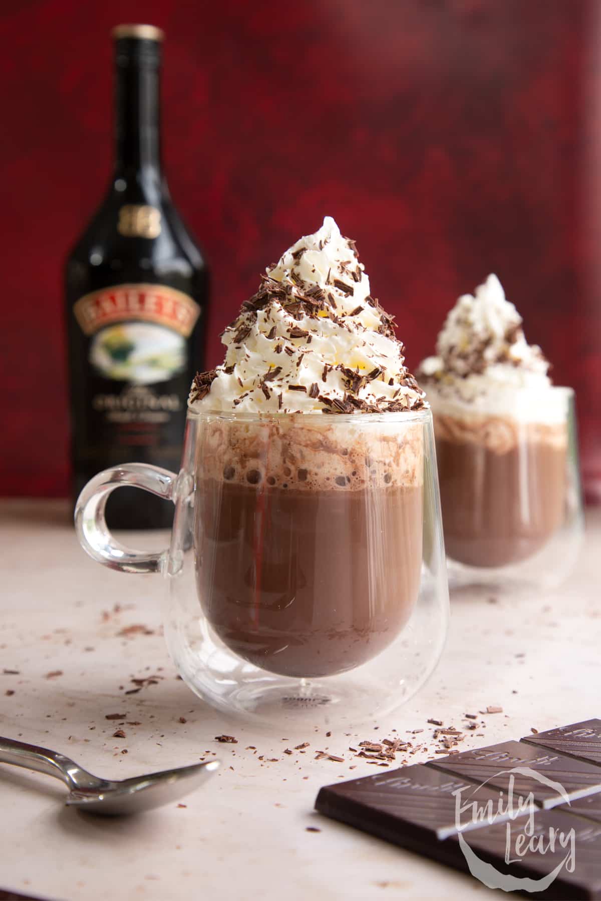Two mugs of a rich Baileys hot chocolate recipe, topped with whipped cream and chocolate shavings.