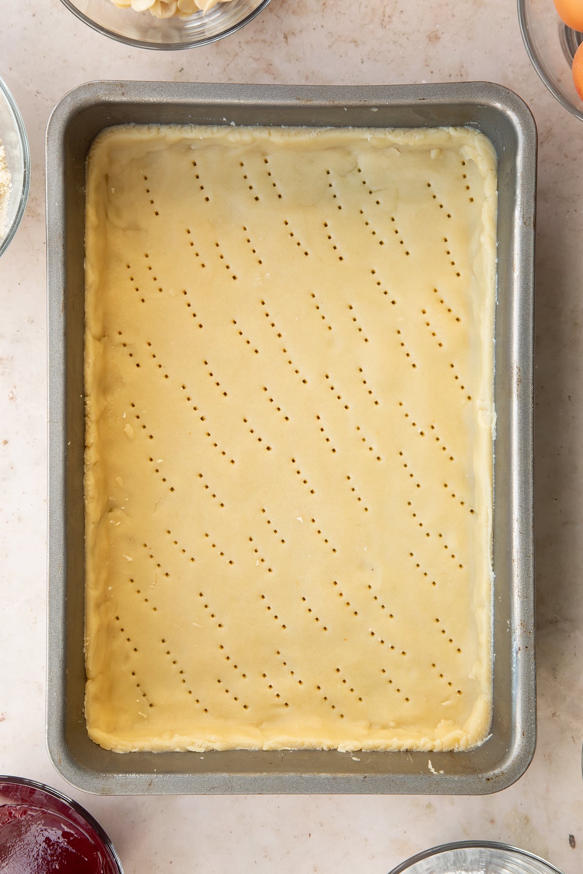 Raw pastry lining the base of a rectangular tin. It has been pricked with a fork.