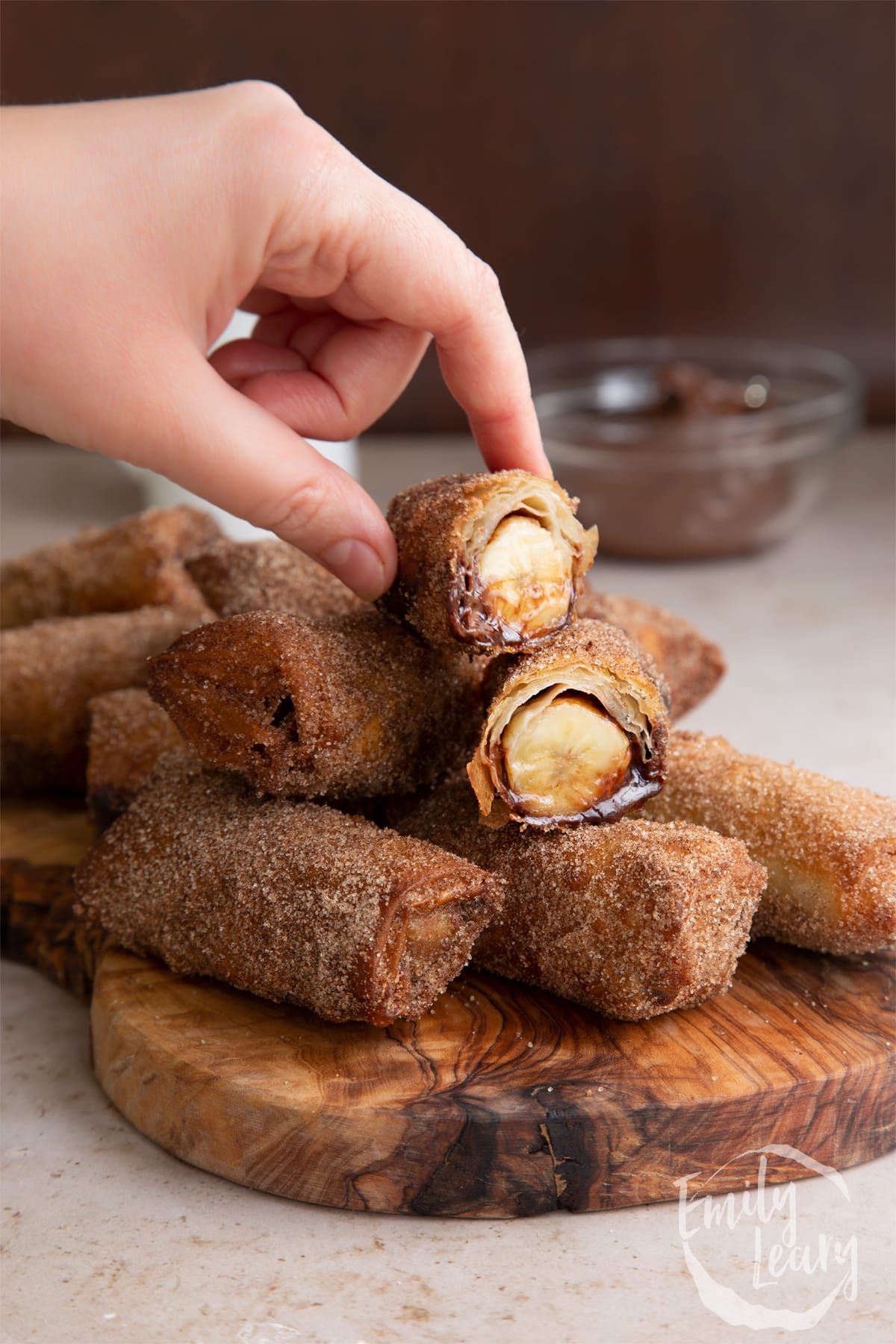 Side on shot of the finished banana chocolate spring rolls on a wooden board with the top roll cut open.