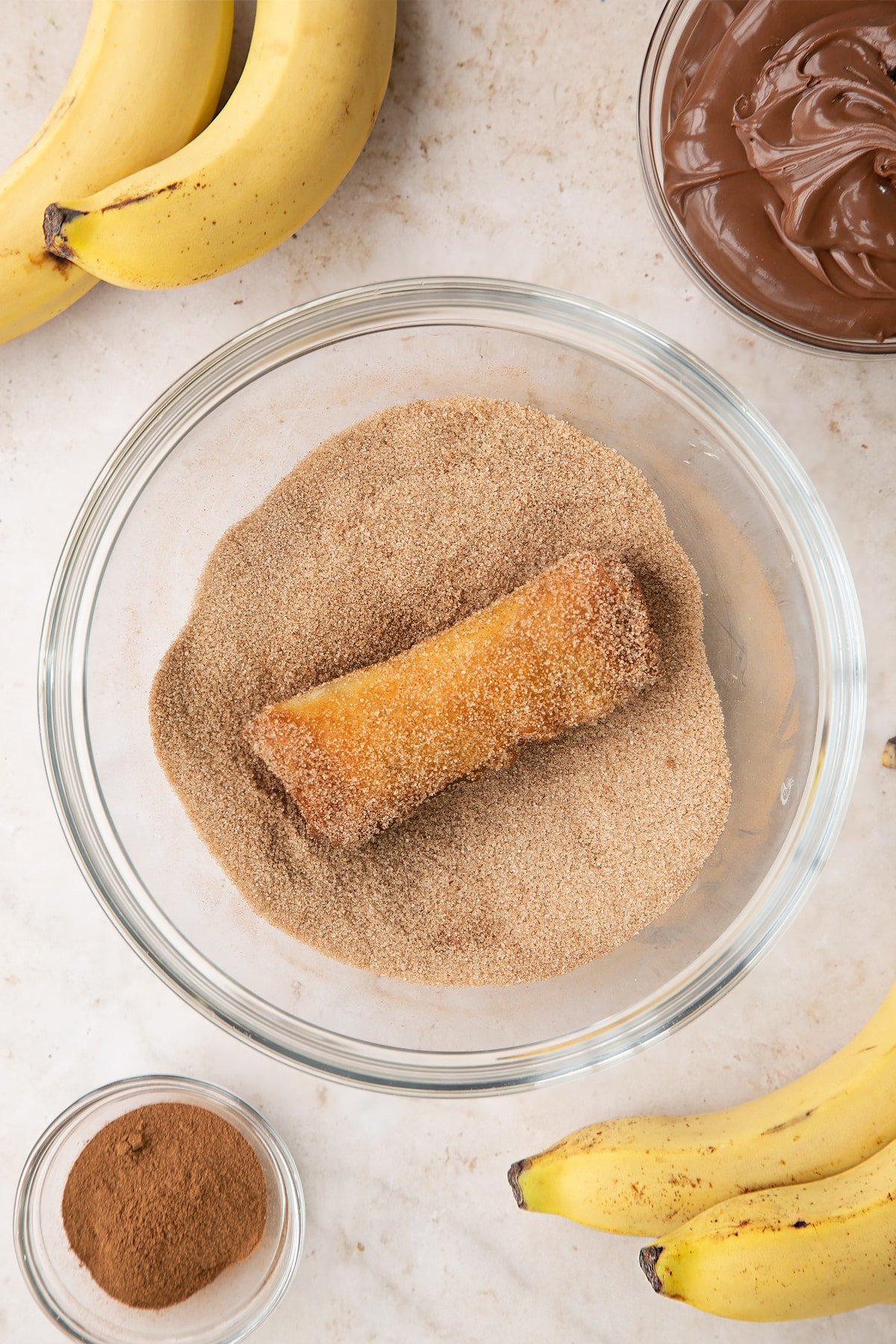 Overhead shot of the banana chocolate spring roll inside a bowl of sugar and cinnamon. 