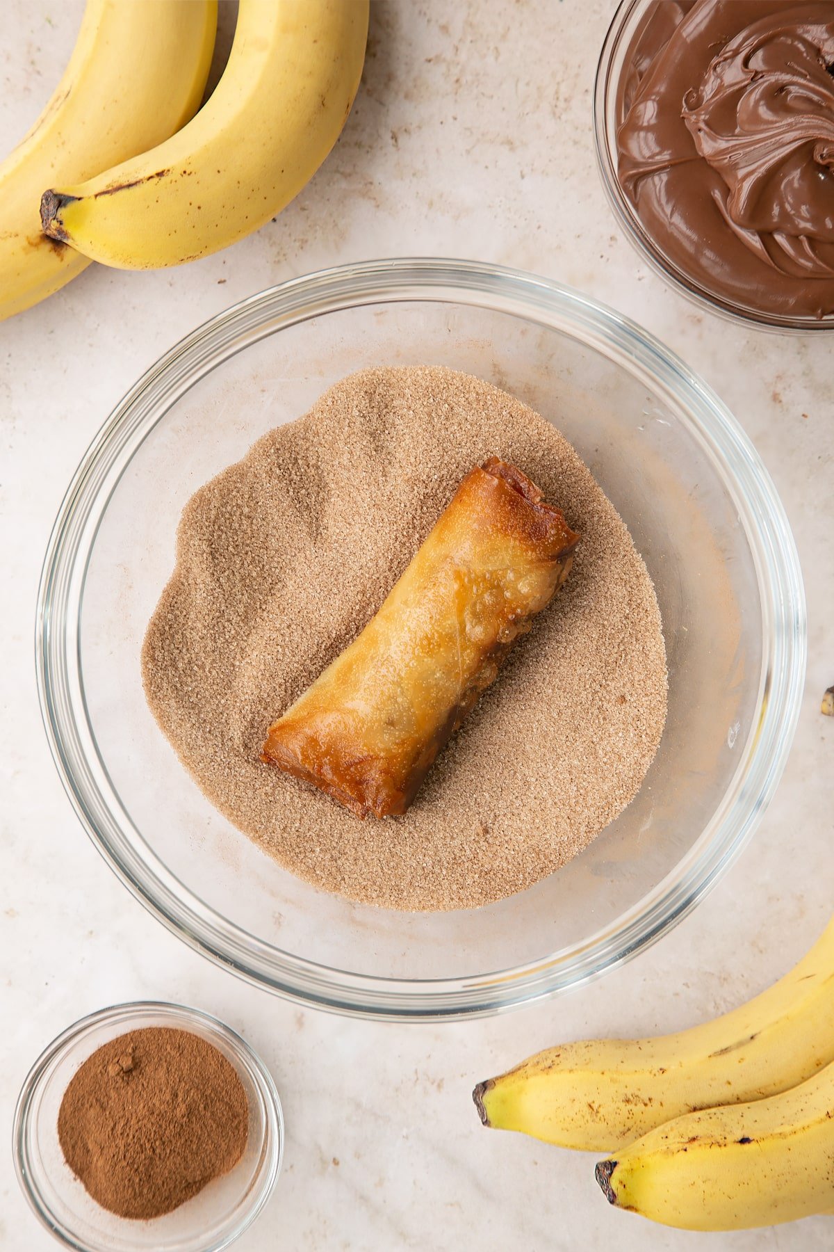 Overhead shot of a banana chocolate spring roll in the cinnamon and sugar mixture.