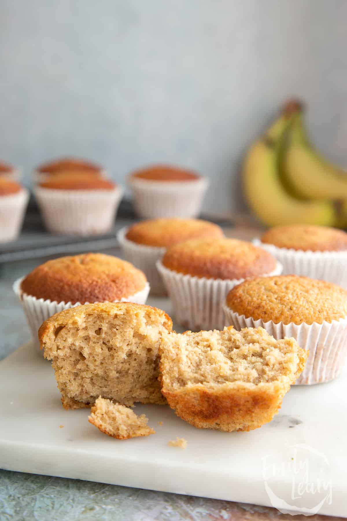 Banana cornmeal muffins on a white marble board. One has been broken open. 